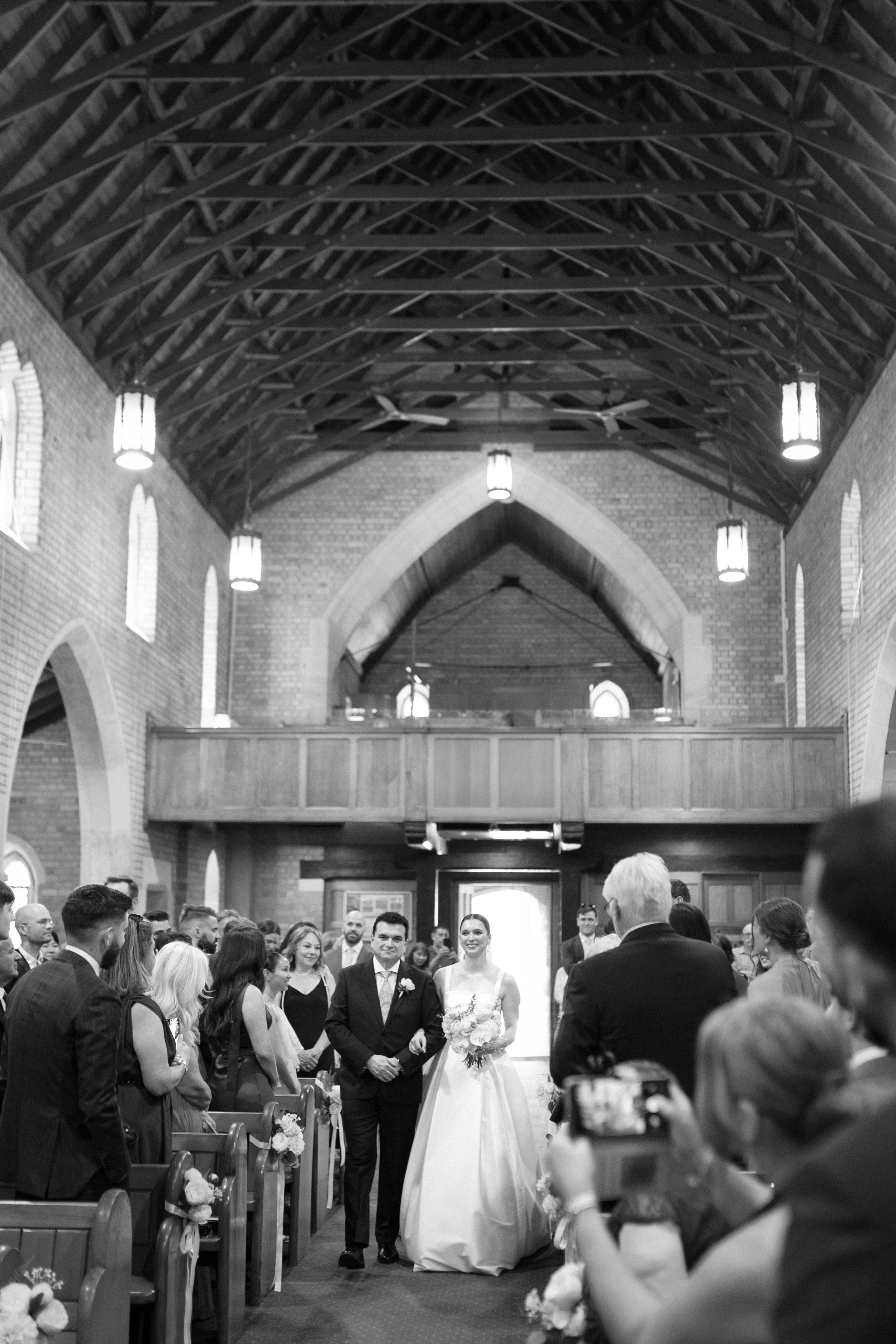 Couple walking down the aisle in a church during their wedding ceremony, surrounded by guests, in black and white.