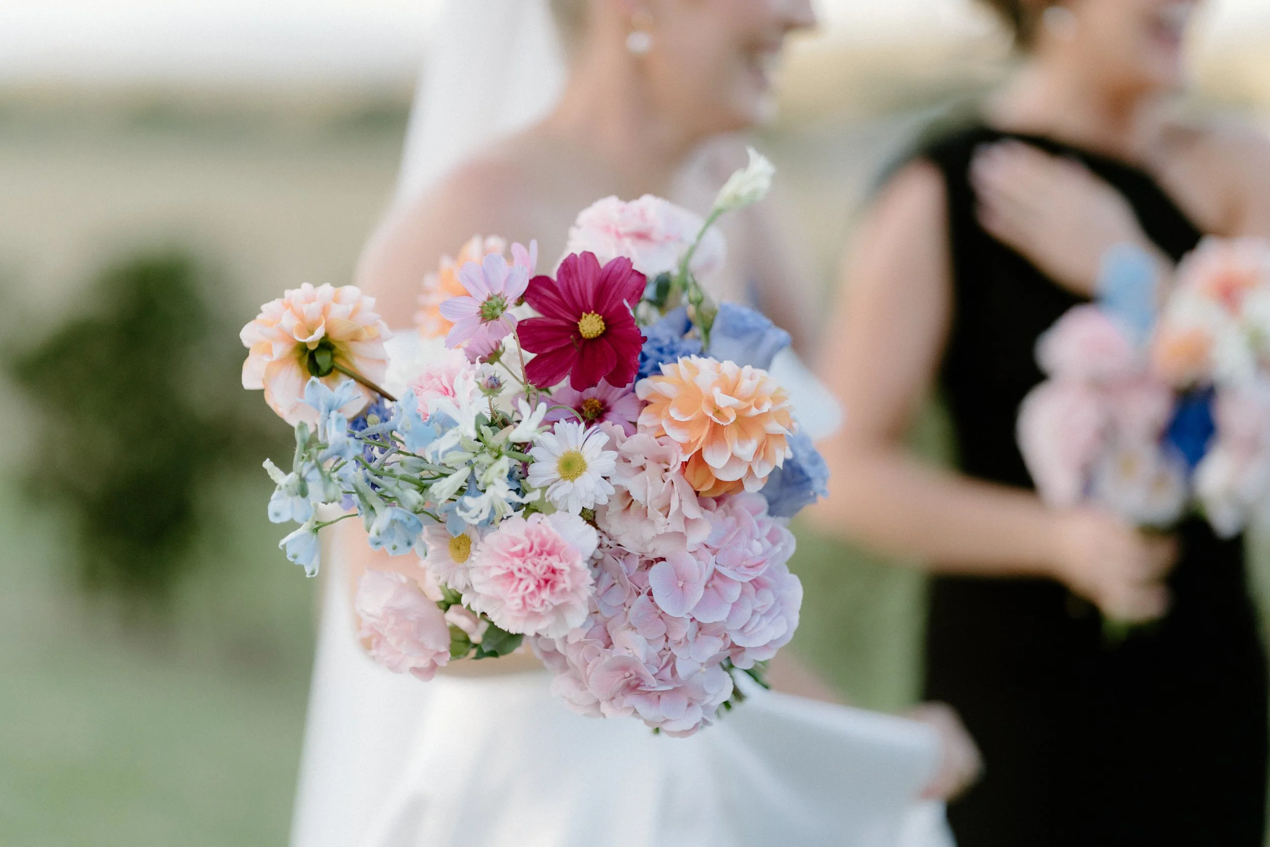 Close-up of a bride holding a colorful bouquet of flowers at a wedding ceremony.