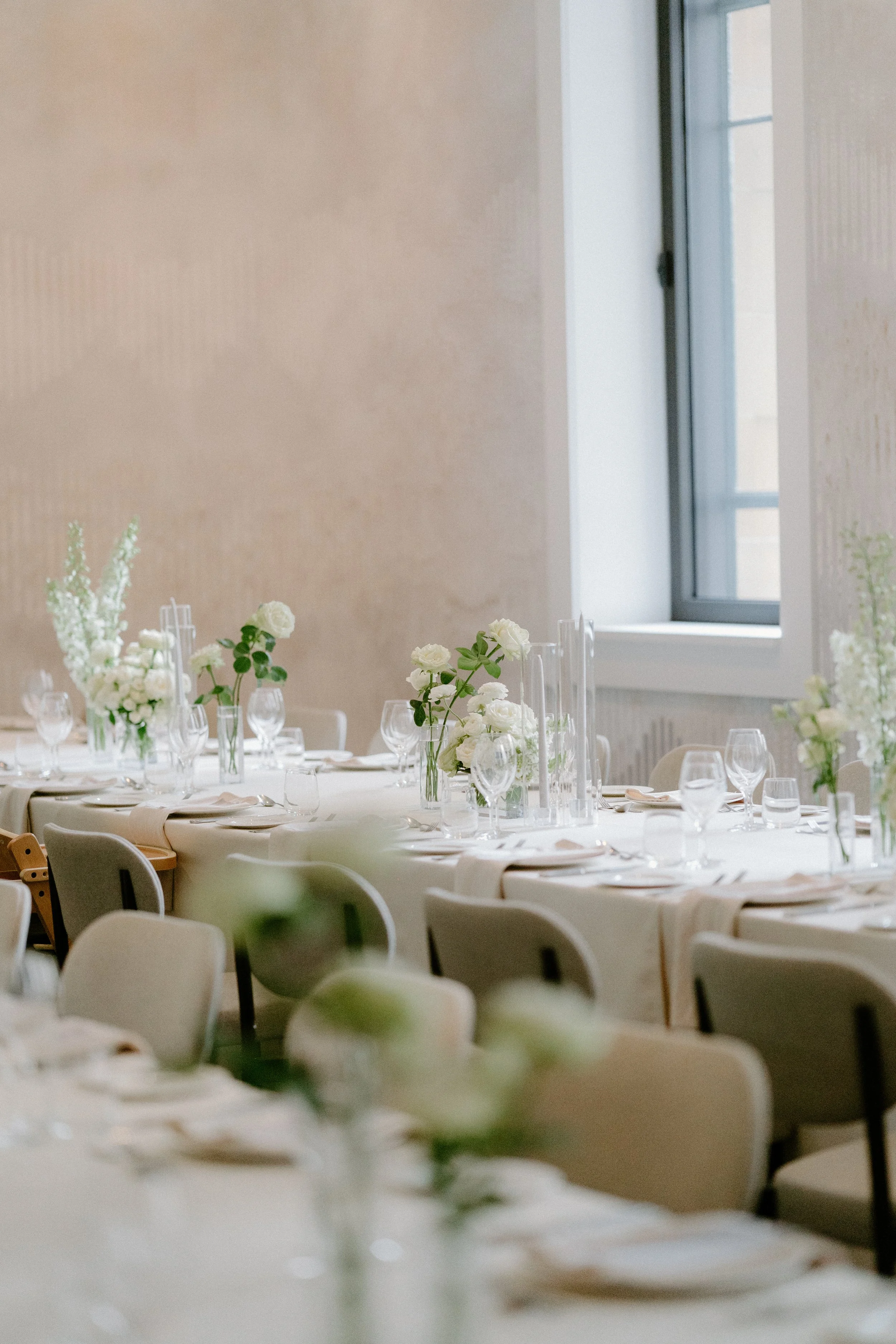 Elegant dining table setup with white flowers and glassware near a window in a decorated event space.