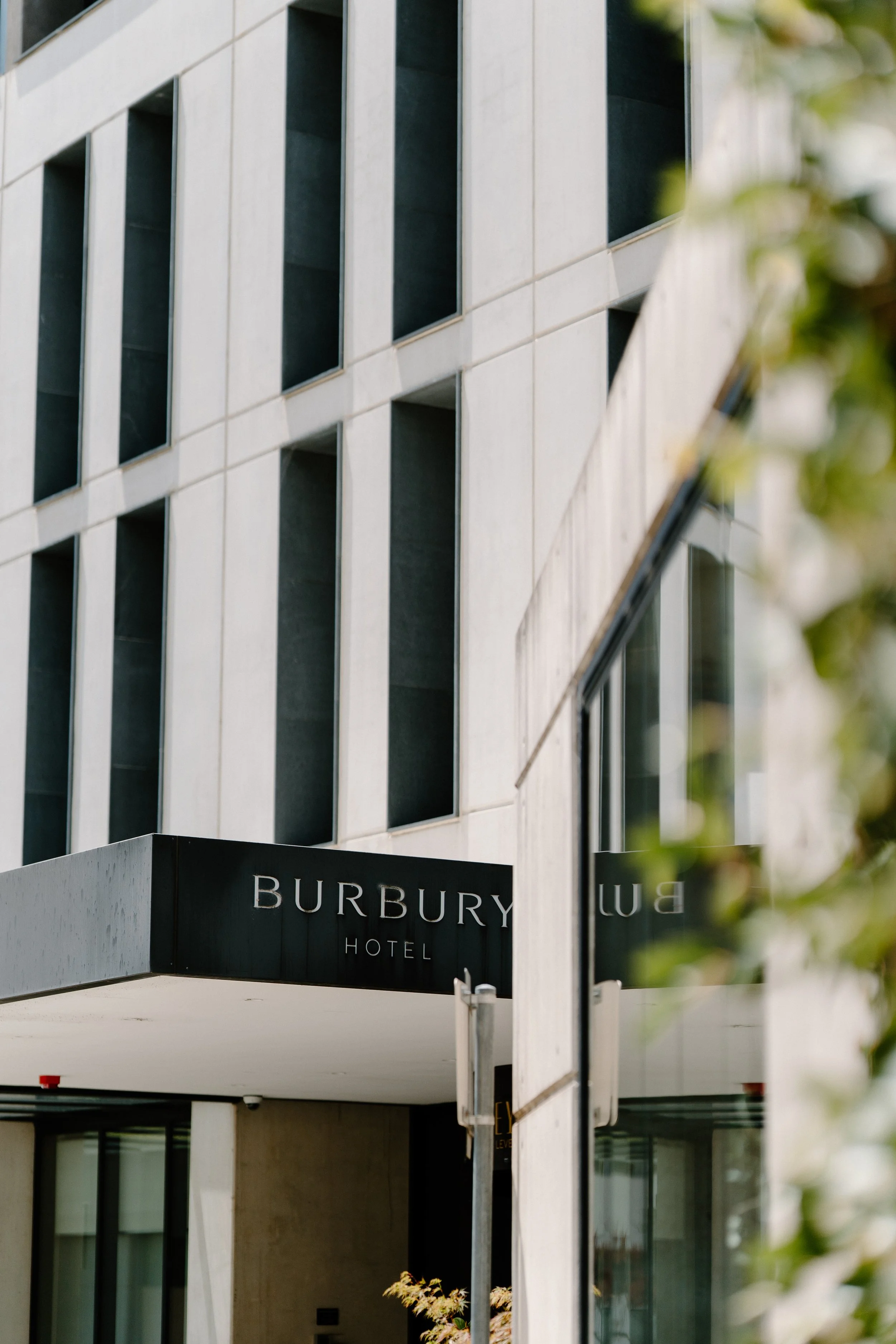 The exterior of the Burbury Hotel building with modern architecture featuring large windows and a black sign with white lettering.