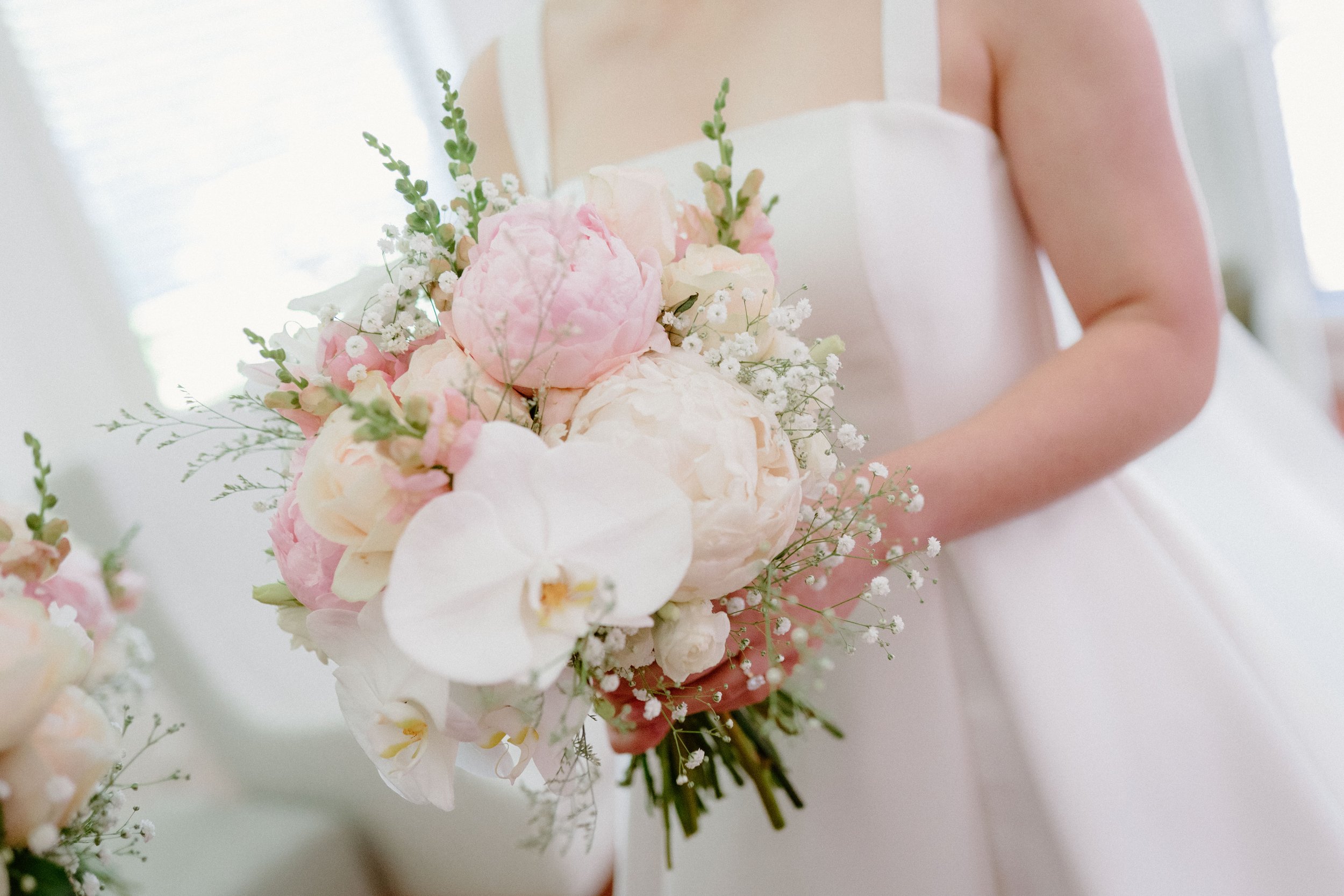 Bride holding a bouquet of pink and white flowers, including orchids and peonies, in a wedding dress.