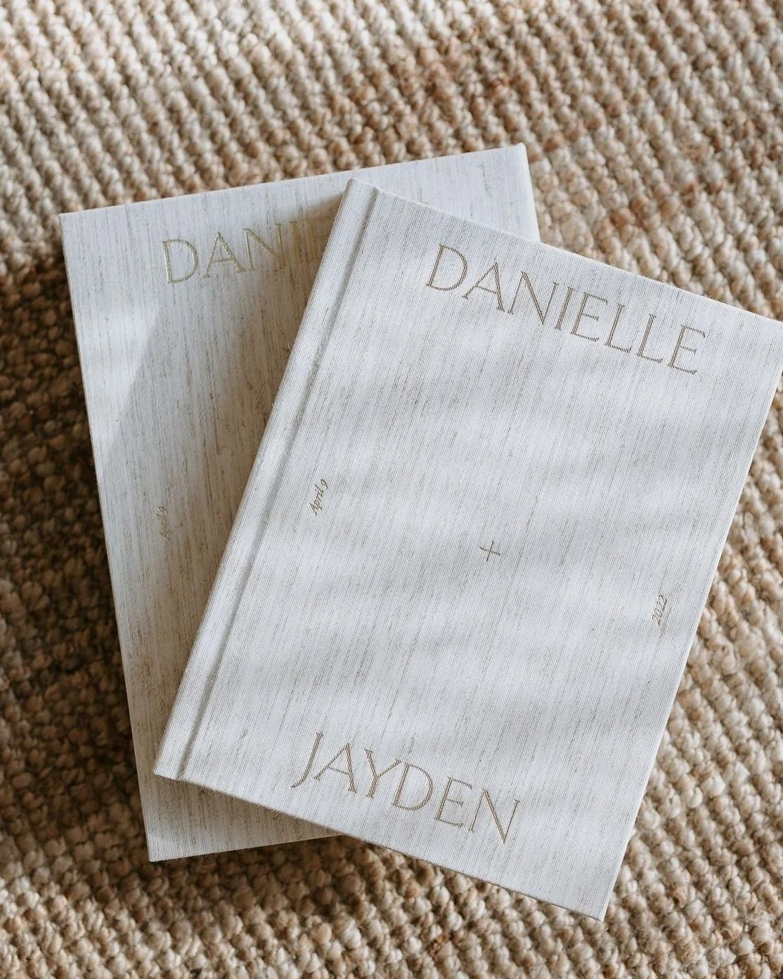 Two white hardcover books with the names Danielle and Jayden on the covers, placed on a textured beige carpet.
