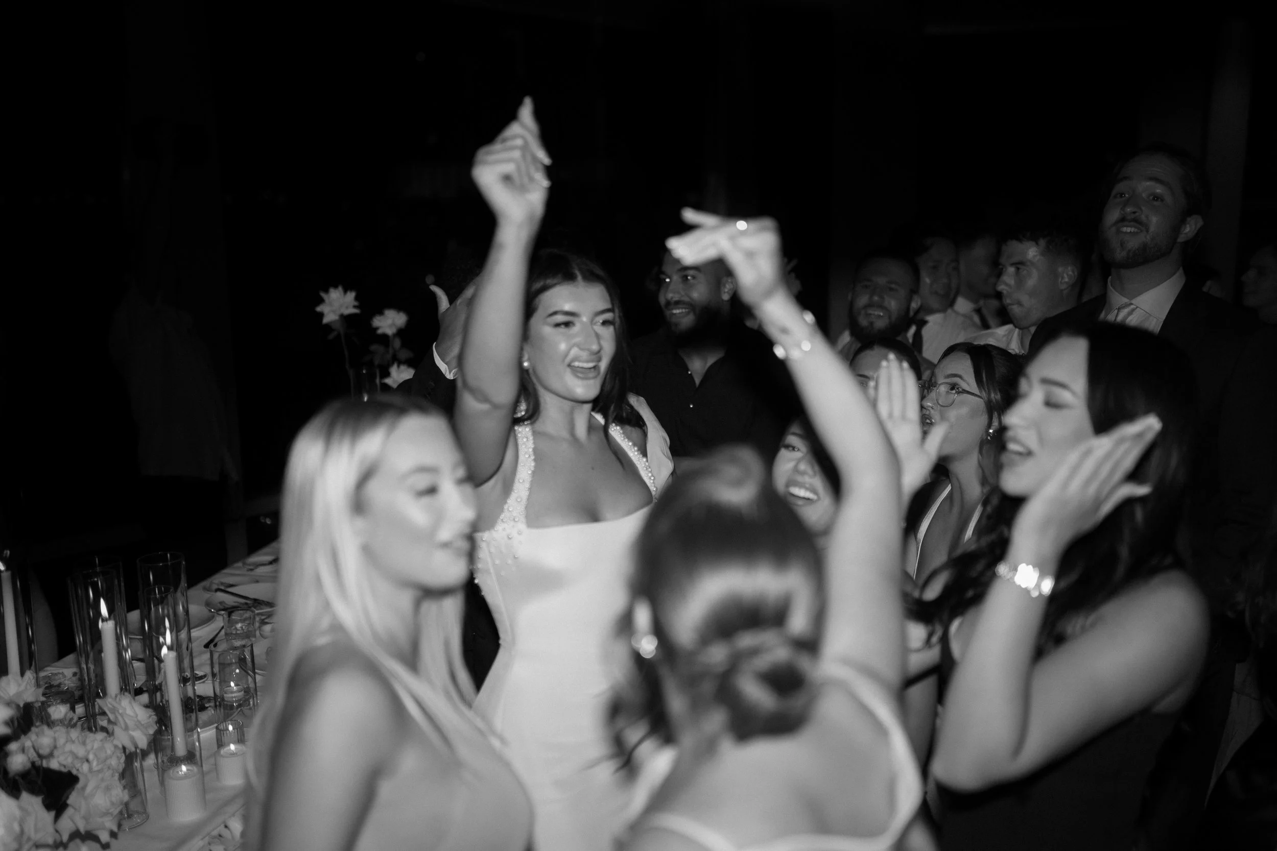 Group of people dancing and celebrating at a wedding reception, with women in the foreground and men in the background.