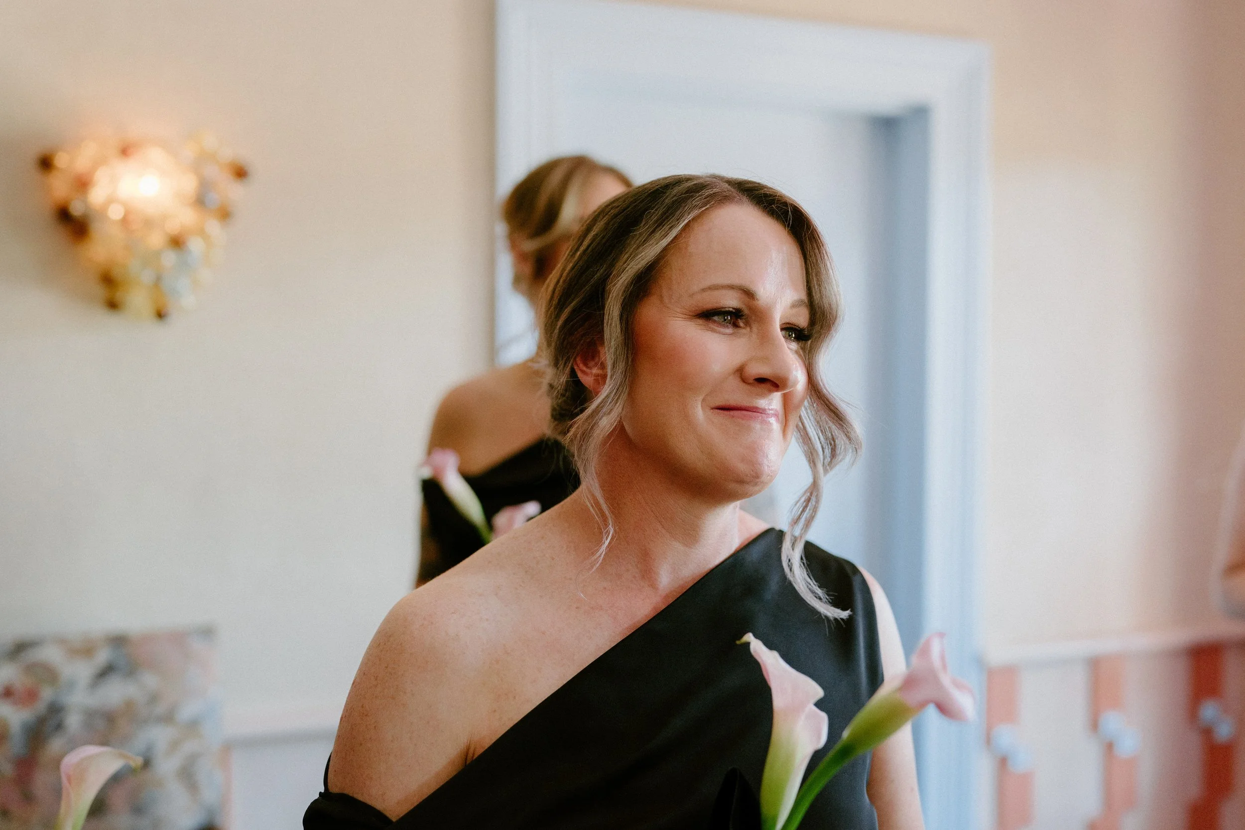 A woman in a black dress looking happy, holding a calla lily flower, in a room decorated for a celebration.
