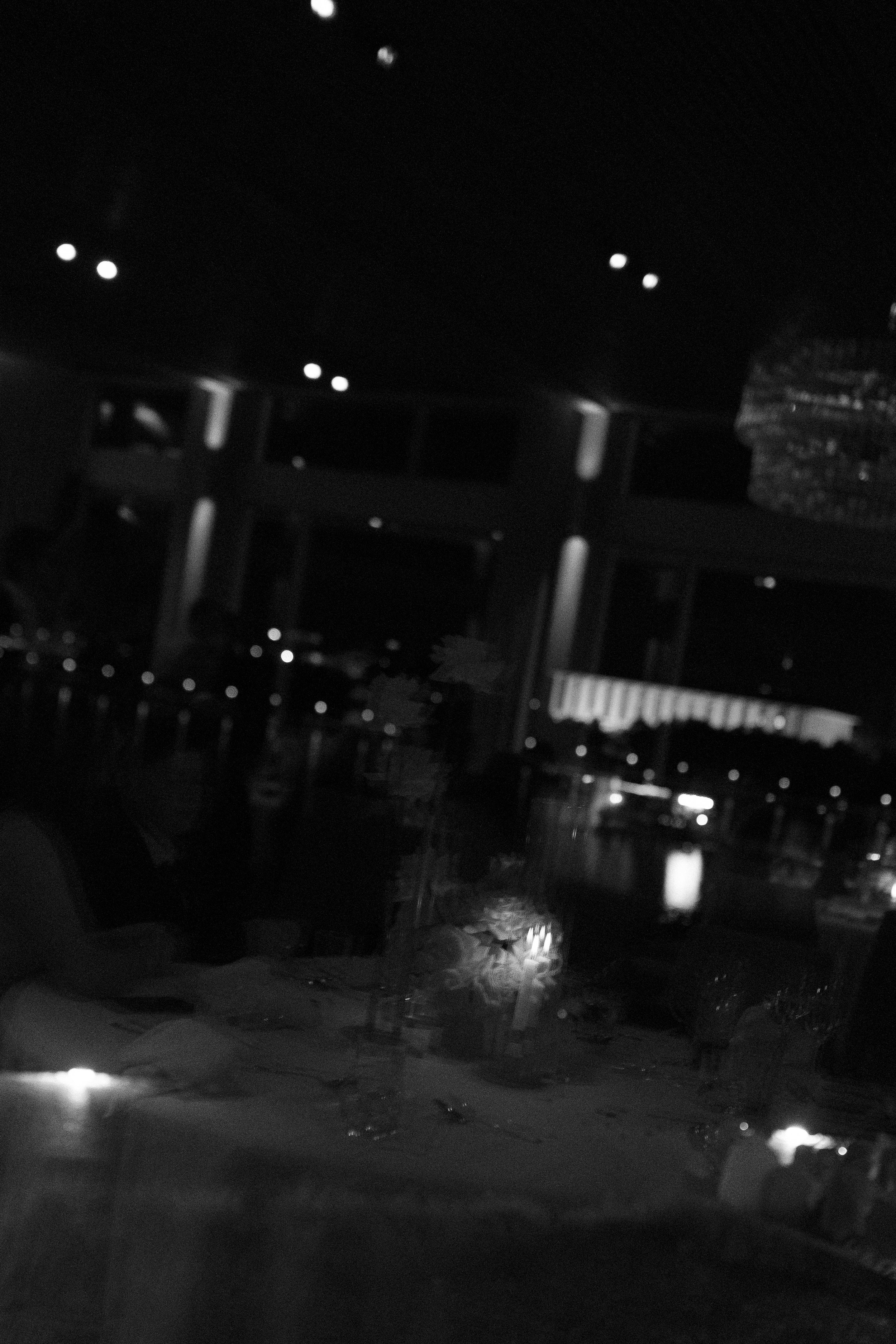 Nighttime scene through a rain-covered window showing a cityscape with lights, buildings, and a bridge or structure.