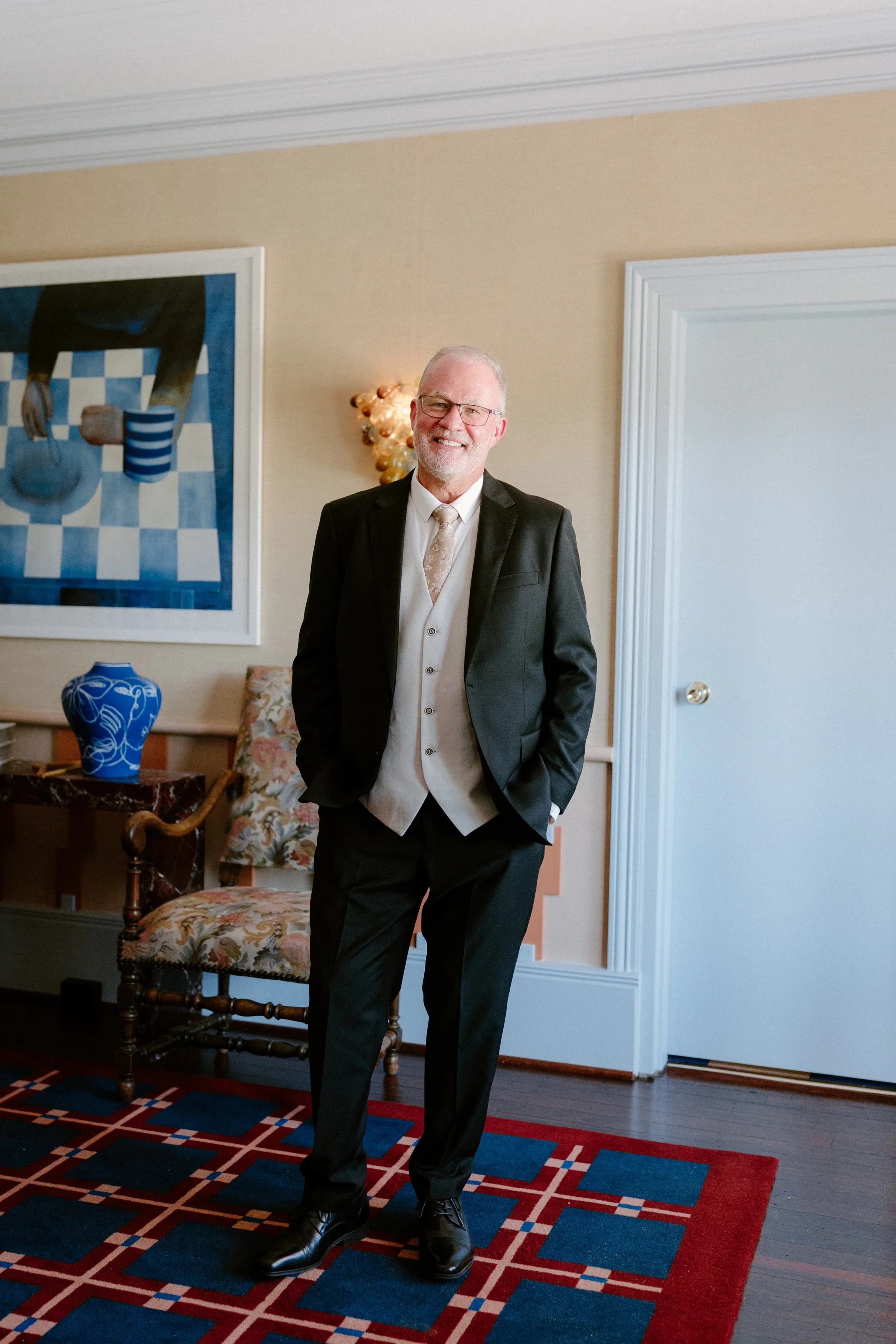 Smiling man in formal attire standing in a decorated room.