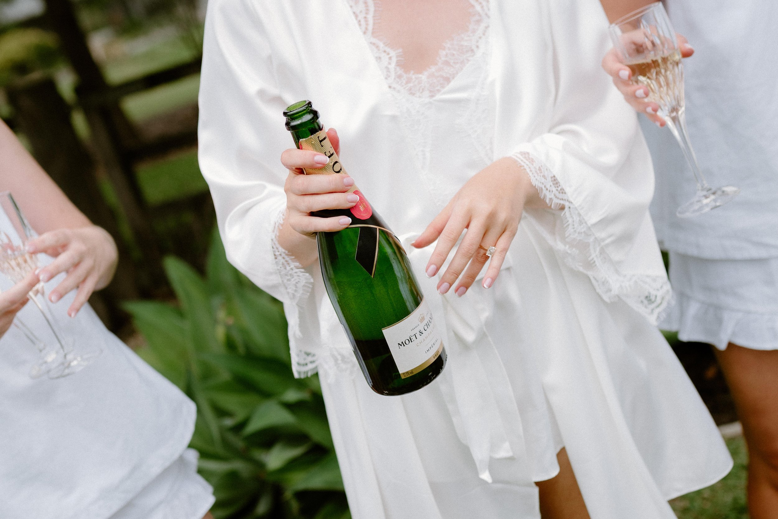 Person in a white dress holding a bottle of Moët & Chandon champagne and a glass of champagne at an outdoor event.