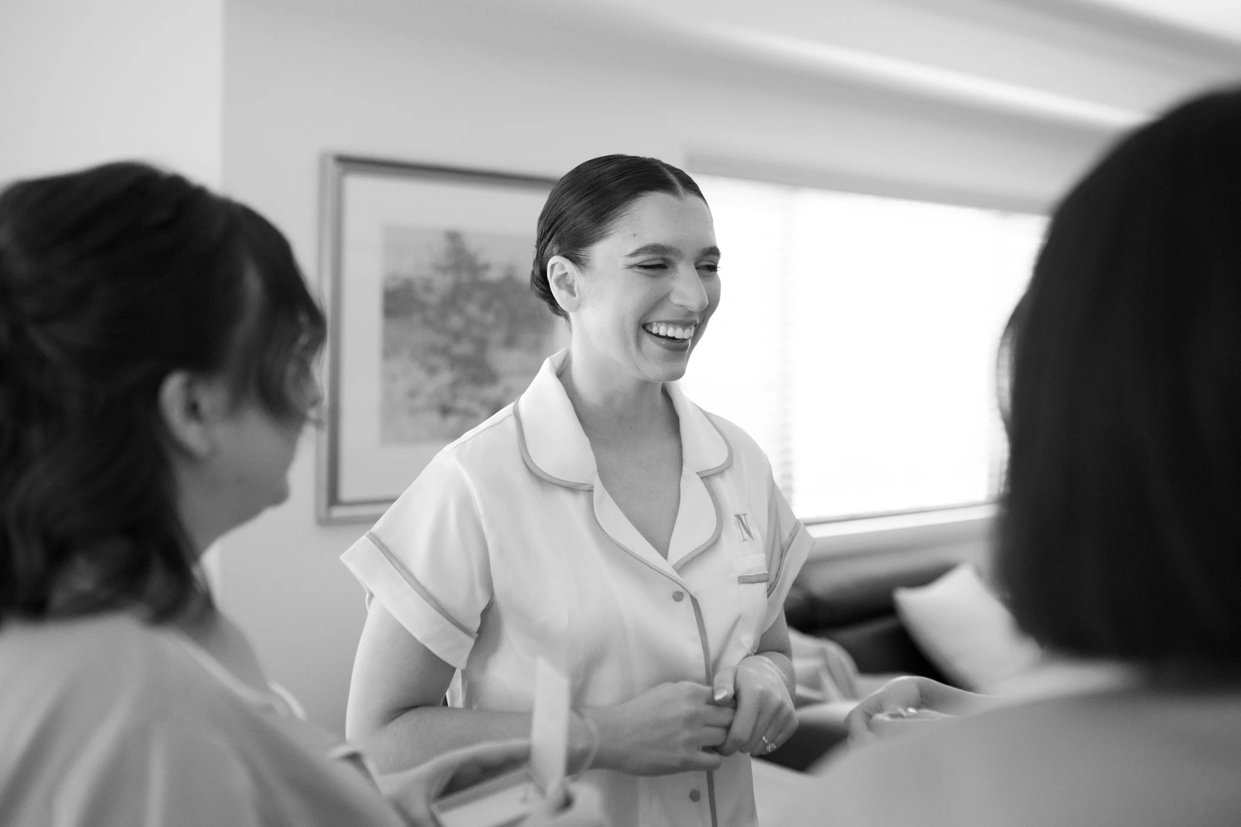 A nurse in uniform laughing and talking with two other nurses in a hospital room.
