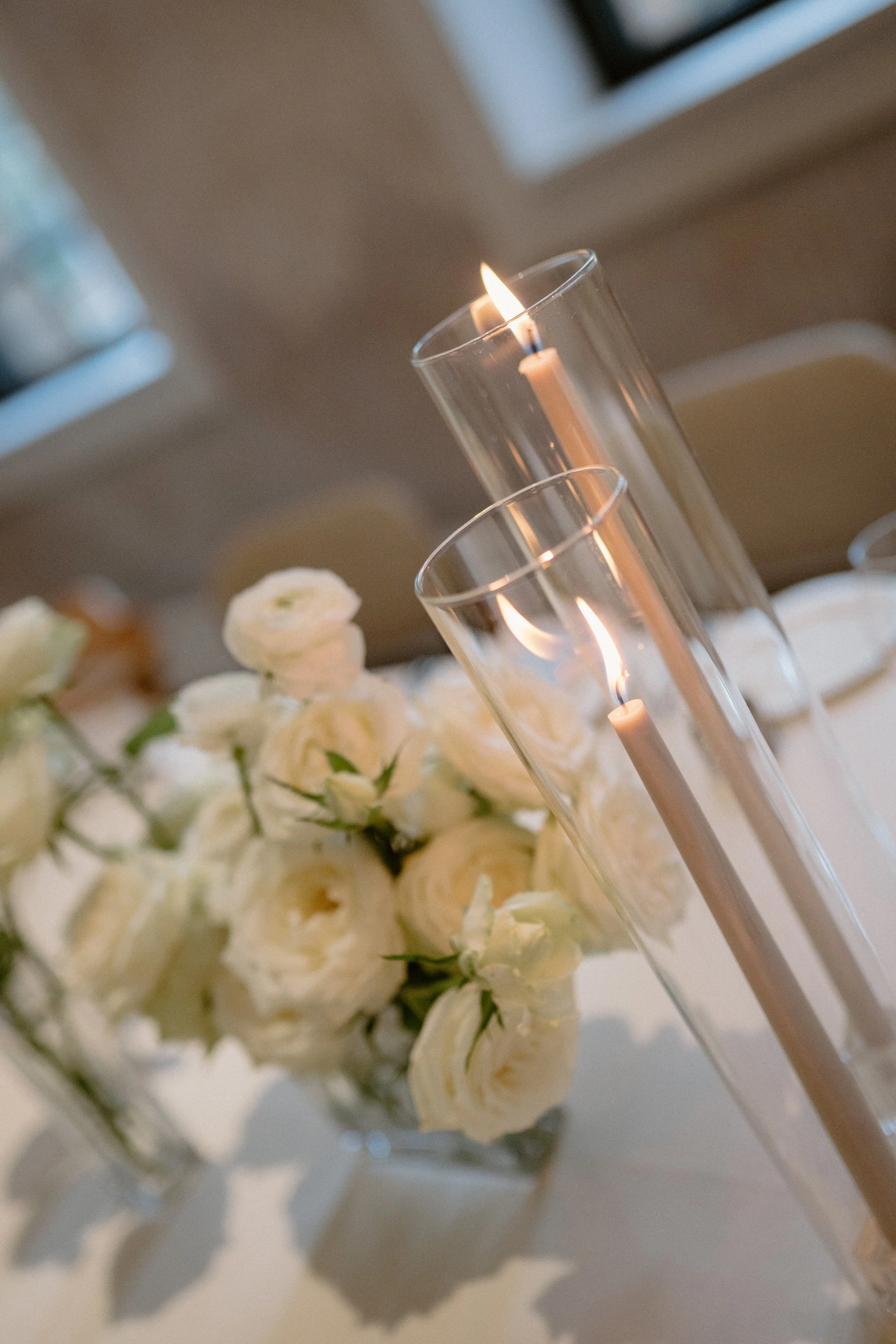 Vase with white roses and two glass candle holders with lit white candles.