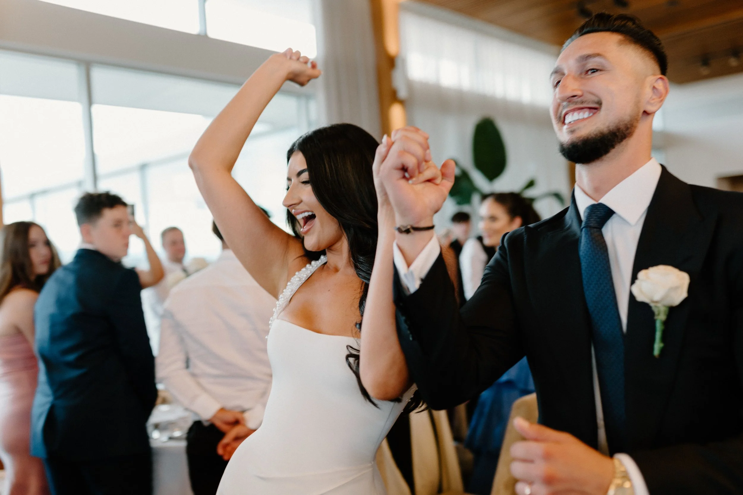 Couple dancing and enjoying themselves at a wedding reception, with several guests in the background.