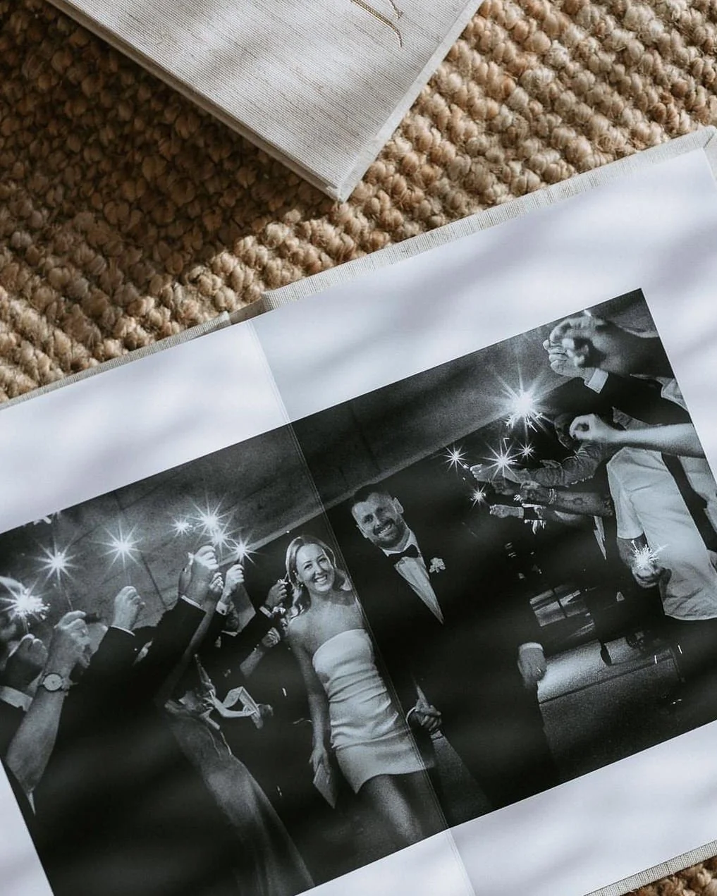 Black and white photo of a wedding reception, with the bride and groom dancing, surrounded by guests holding sparklers.