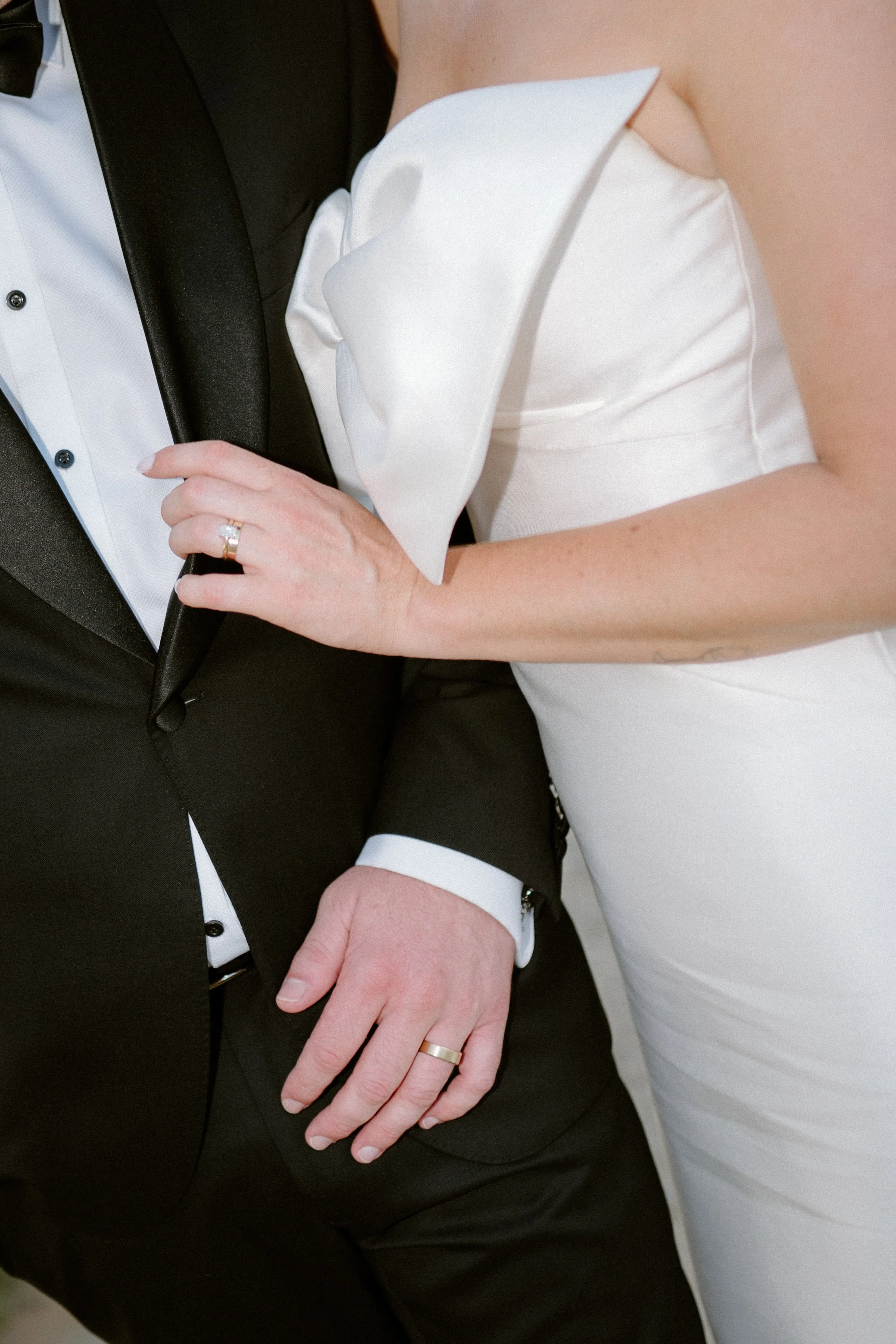 The Sienna, Hunter Valley Wedding Venue, Wedding Photos. A close-up of a bride and groom on their wedding day. The bride is wearing a white wedding dress, and the groom is in a black tuxedo. The bride is resting her hand with a wedding ring on the gr