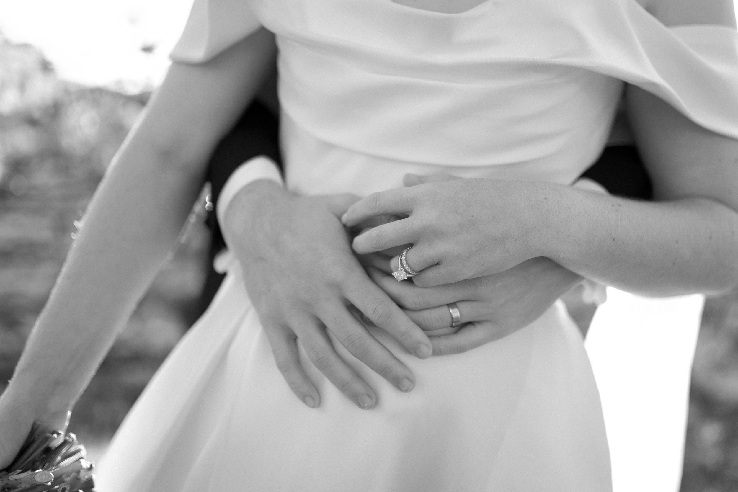 Black and white photo of two people holding hands, one with a ring on the ring finger, suggesting a wedding or engagement.