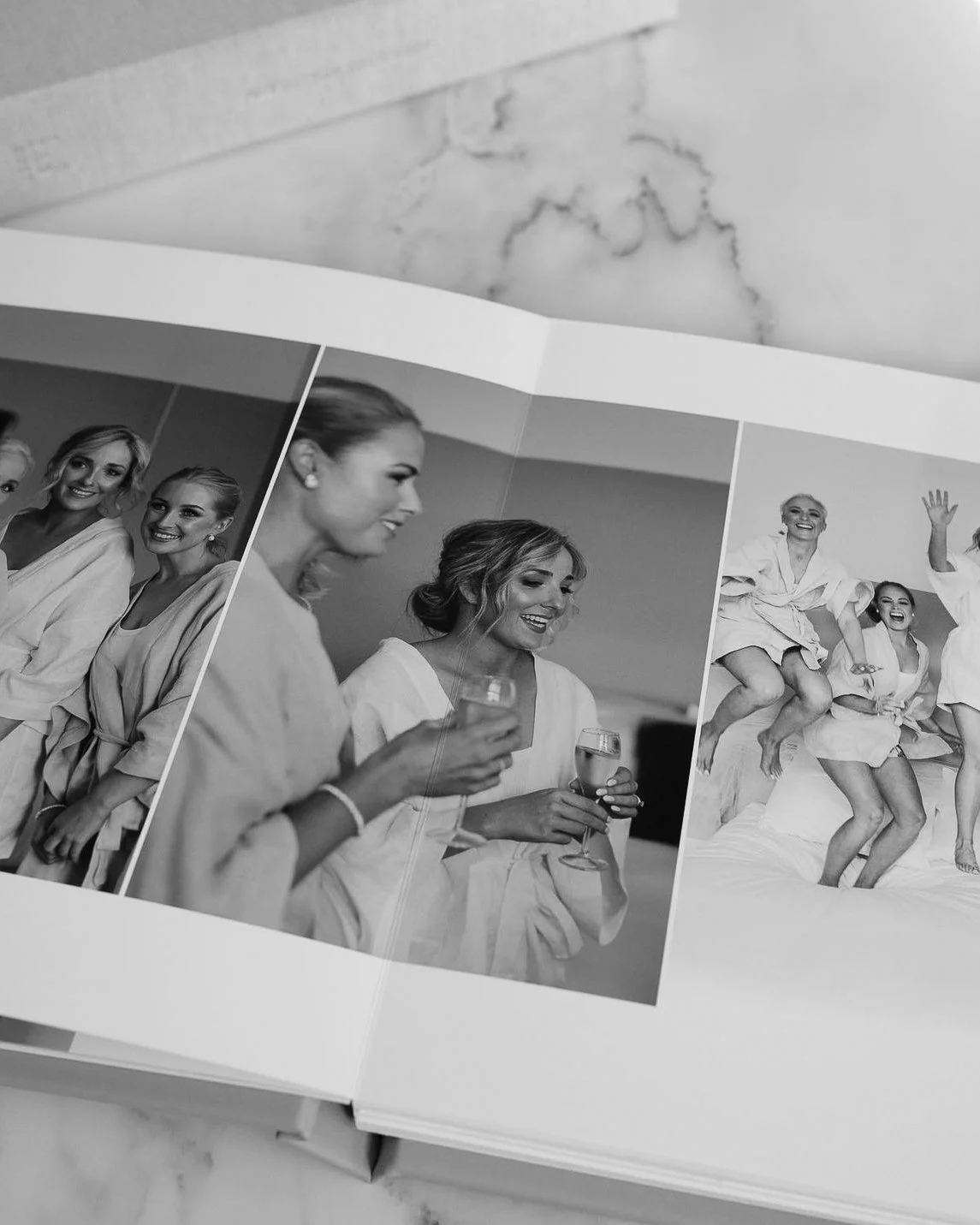 Black and white photo album open to two pages featuring women in robes celebrating with drinks and jumping on a bed.