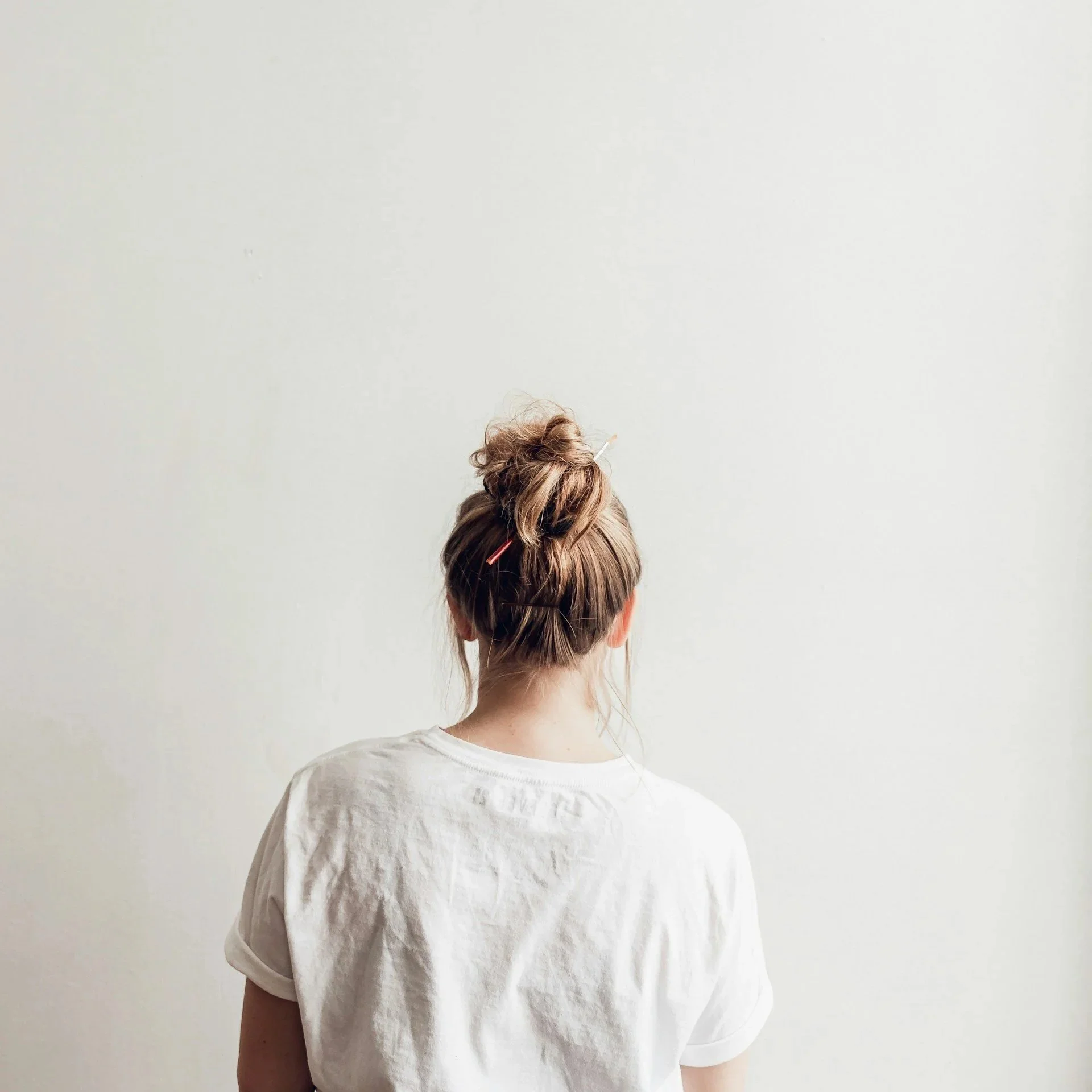 Portrait de dos d’une femme en t-shirt blanc face à un mur clair — posture naturelle et calme