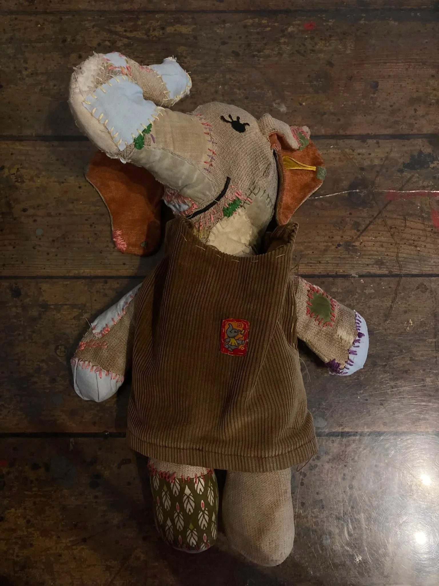 Ein Stoff-Stuben-Puppe mit buntem Kleidung, die auf einem Holzboden liegt.