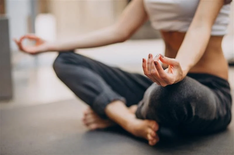 Person sitting cross-legged on the floor in a yoga pose, with one hand in a mudra gesture.