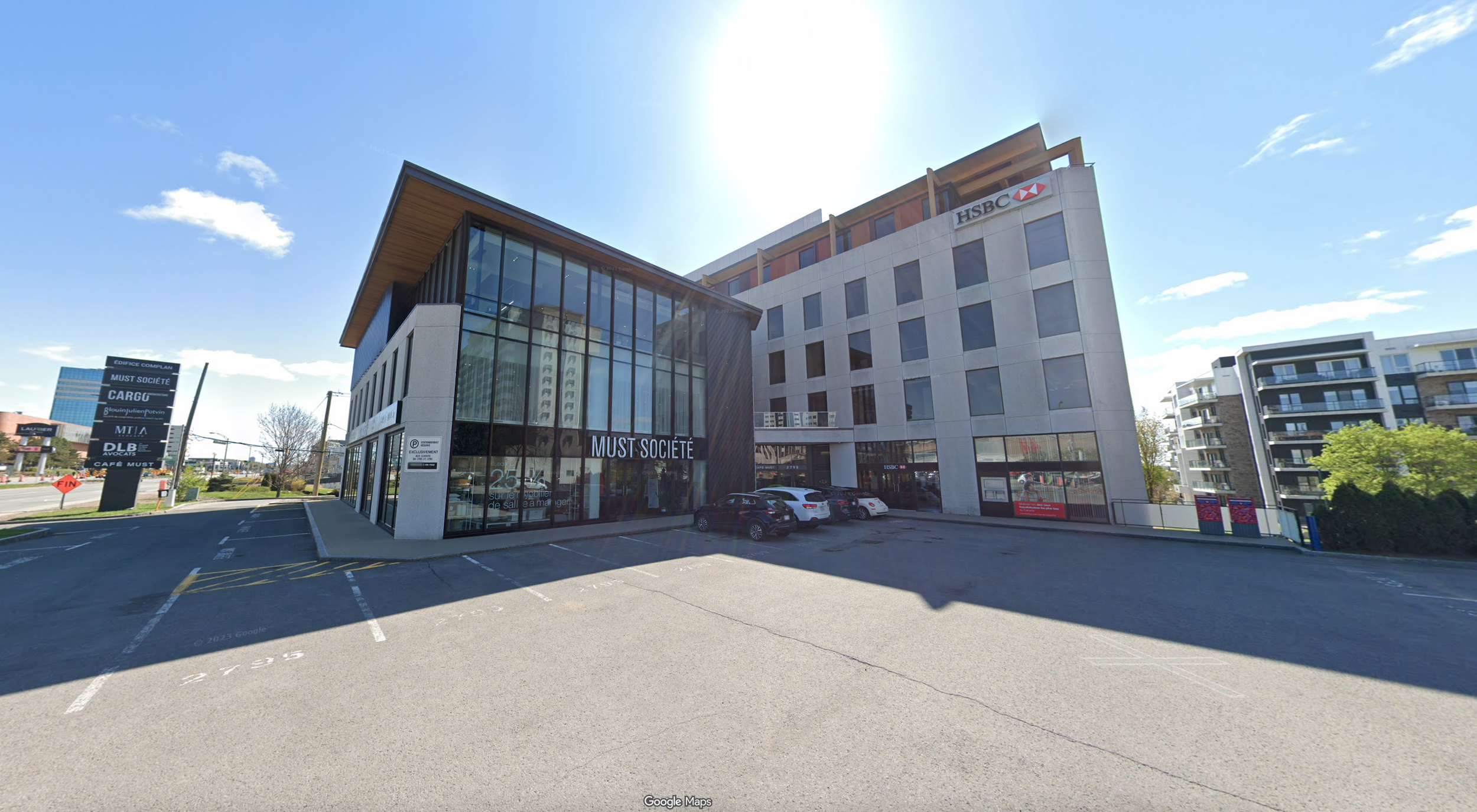 Bâtiment de bureaux moderne avec des fenêtres en verre et des voitures garées devant, branding pour 'Must Société' et 'HSBC'
