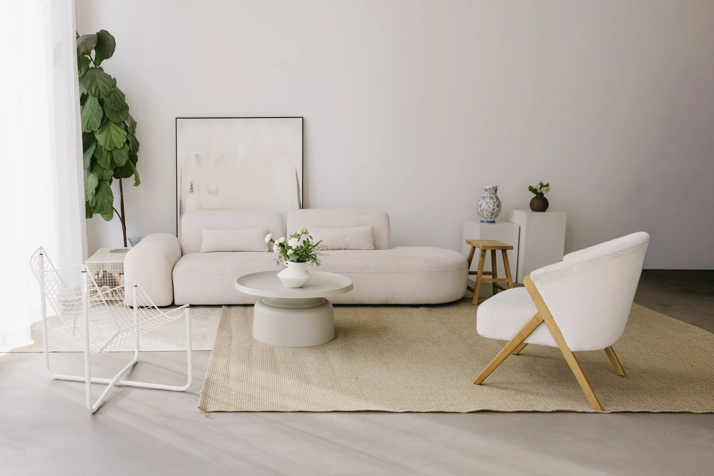 Un salon minimaliste avec un canapé blanc, une table basse et une chaise blanche avec pieds en bois, décoré avec des plantes et des vases