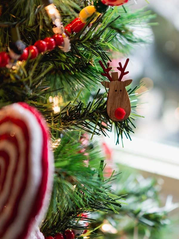 A closeup shot of a wooden reindeer Christmas ornament on the branch of a Christmas tree.