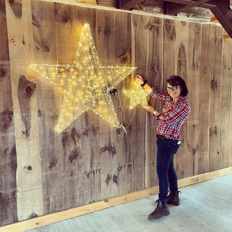 Stouffville Christmas Home Tour volunteer Carolyn installs lighted stars on a wooden wall in the barn