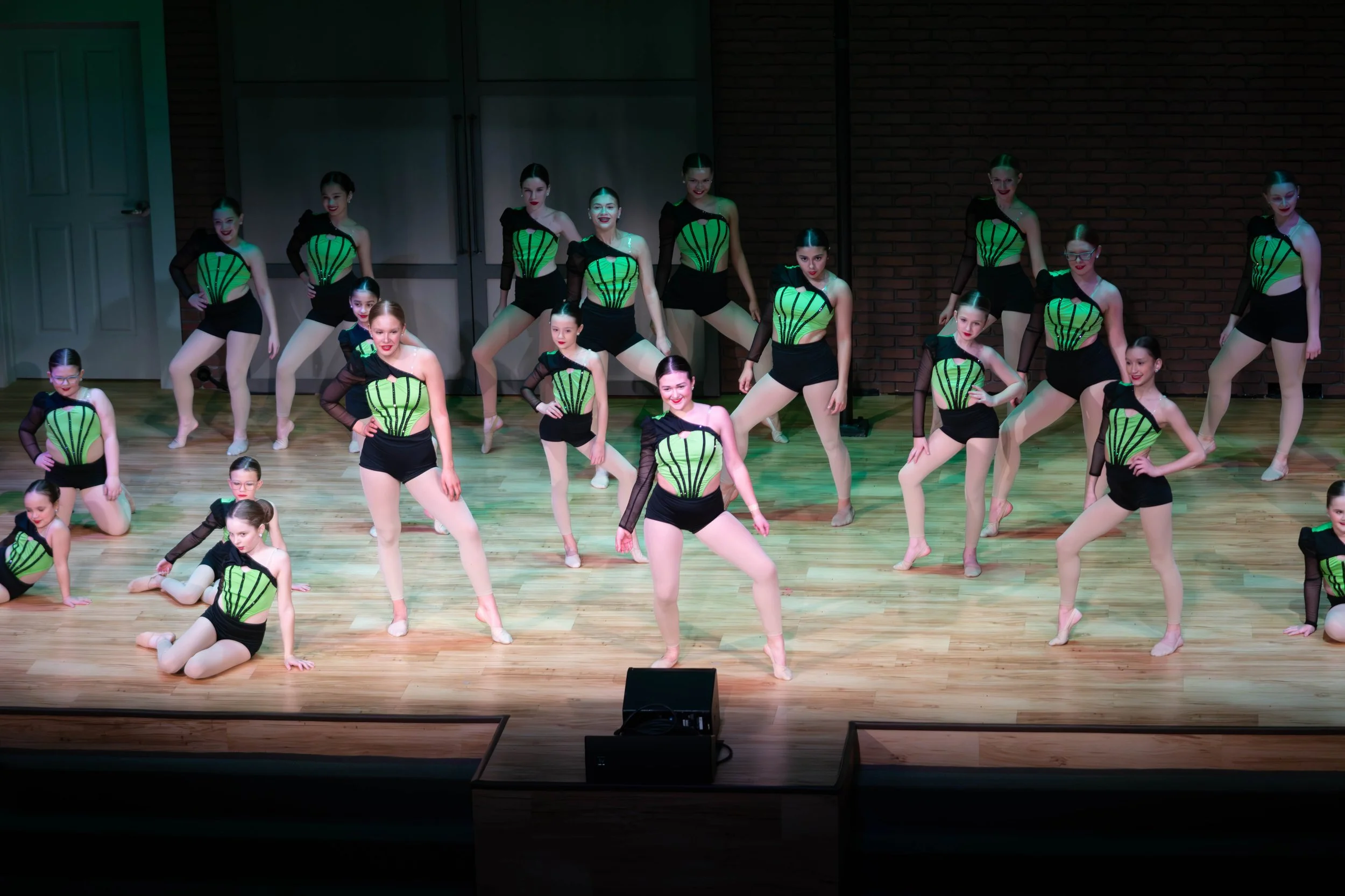 Young female dancers in matching green and black costumes performing a group routine on stage at Relevé Dance Company® recital