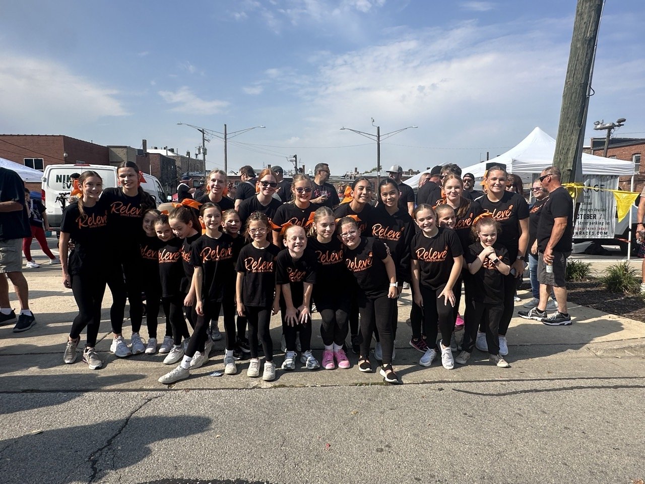 Dance team from Relevé Dance Company representing Lockport, Homer Glen, and Lemont areas posing together outdoors in matching black ‘Relevé’ shirts during a community event.