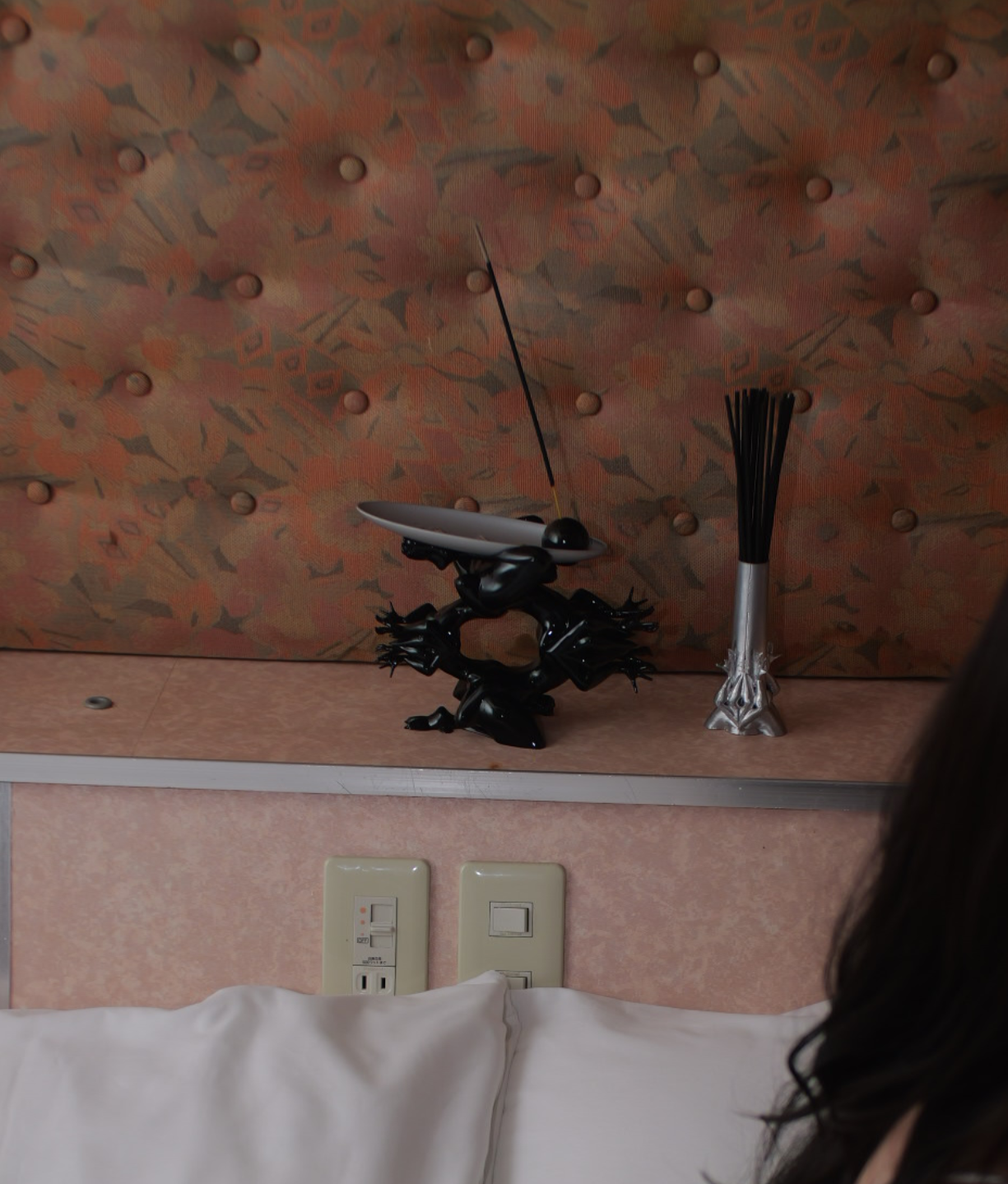 Decorative wall shelf with black frog-shaped base, a silver dish with a black sphere, a black antenna, and a silver-and-black vase, in front of a padded, patterned wall.
