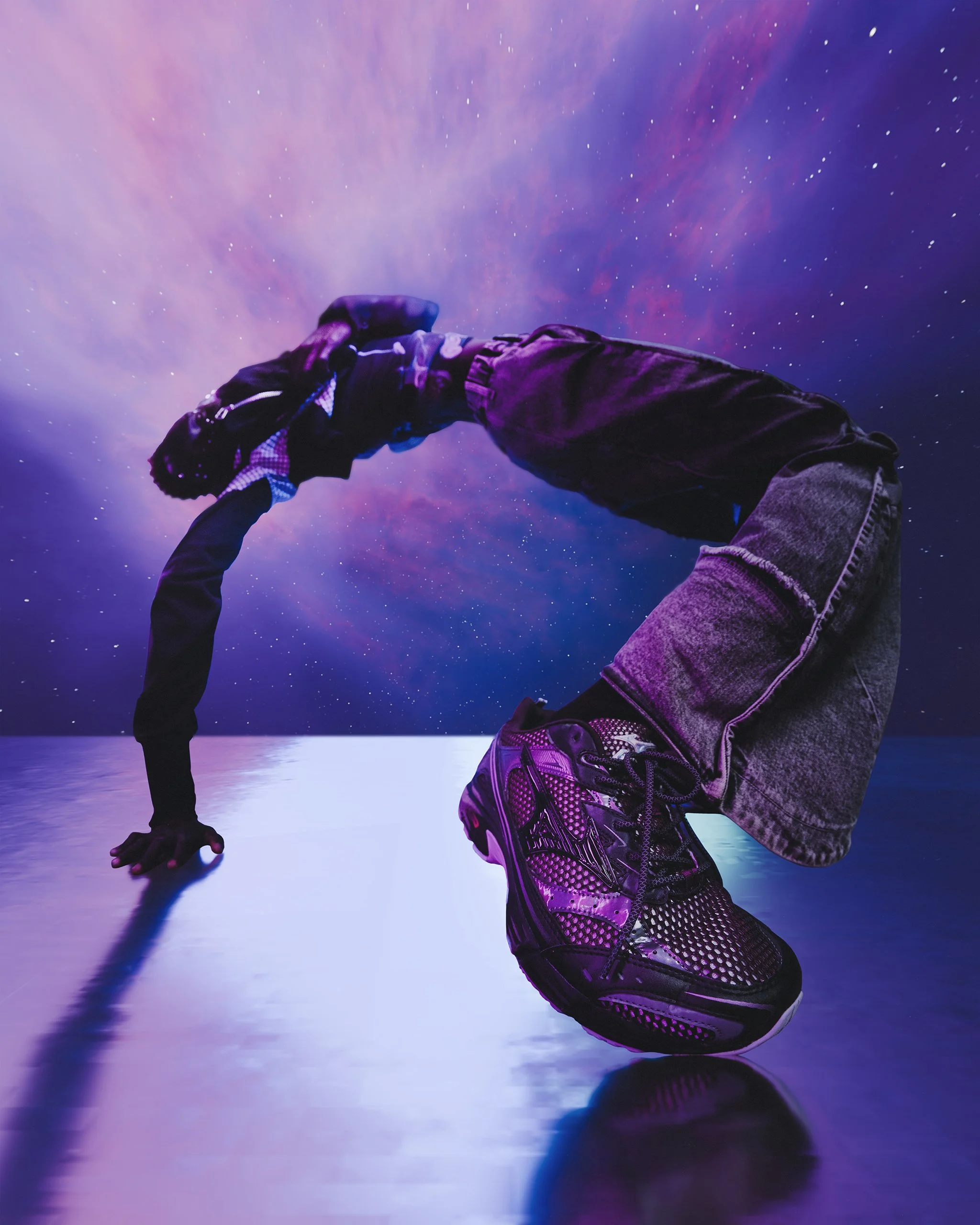 A person performing a handstand against a colorful cosmic background with stars, with one foot on a reflective surface.