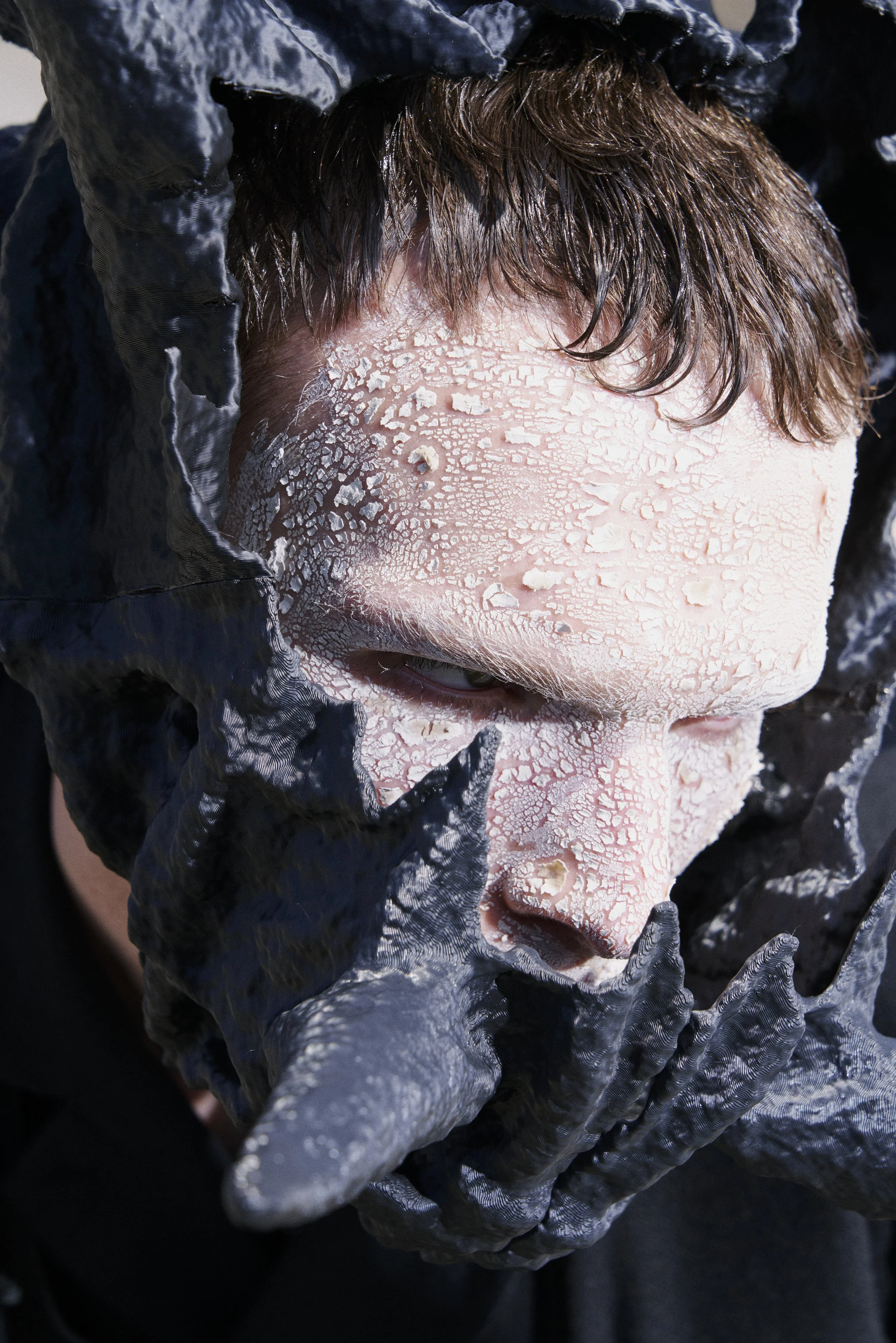 A person with white cracked facial mask and black gloves, partially covering their face and head.