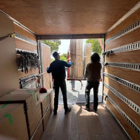 Atthowe art handlers loading artwork into a climate-controlled truck, with wall-mounted rigging straps visible to the left near other secured crates of art.