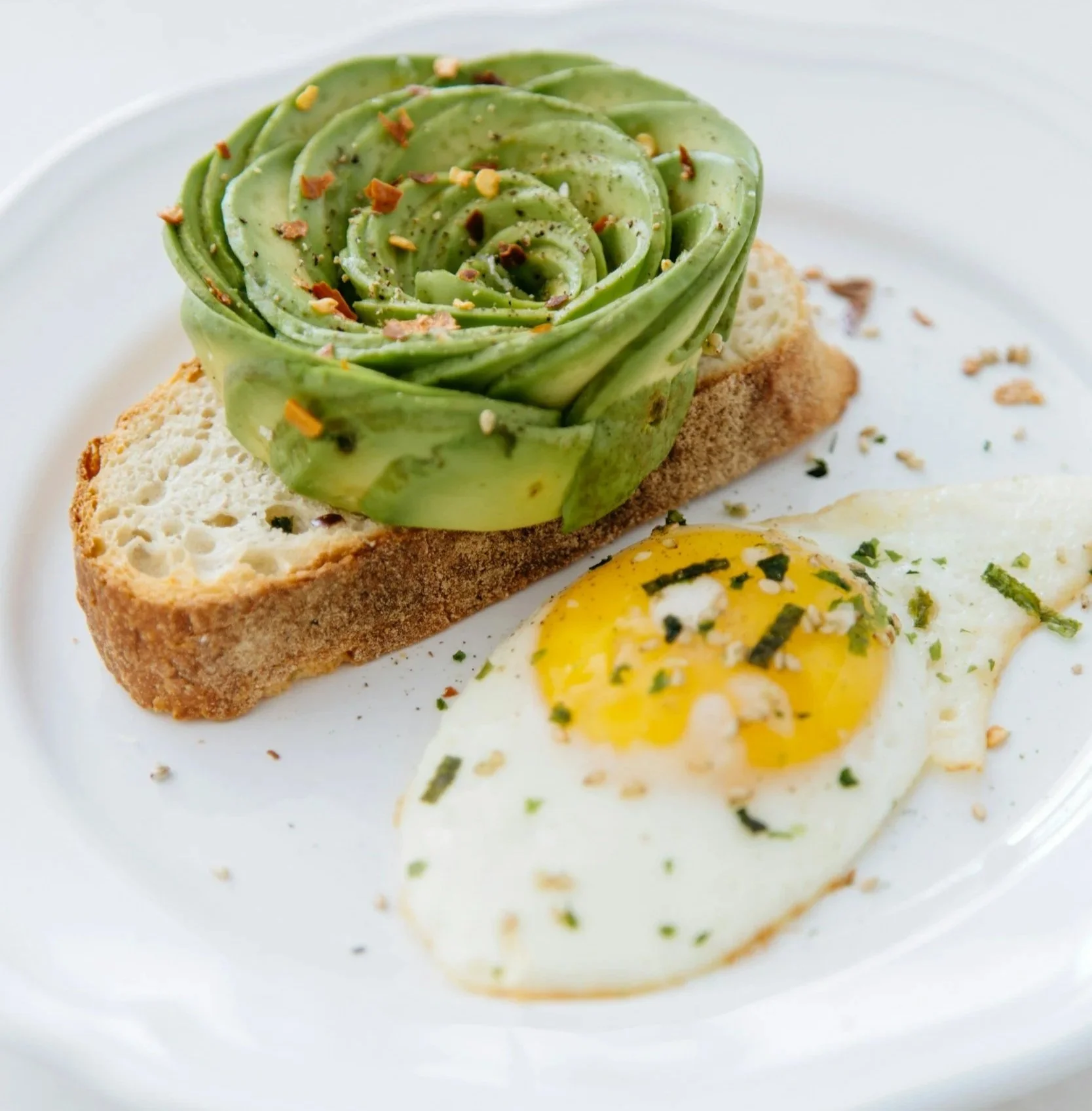 Assorted peaches on a white surface, some on a wooden board, a white bowl, and green leafy branches with white flowers.