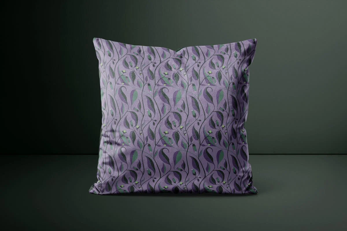 A purple decorative pillow with a leafy vine pattern in shades of green and black, set against a dark gray background.