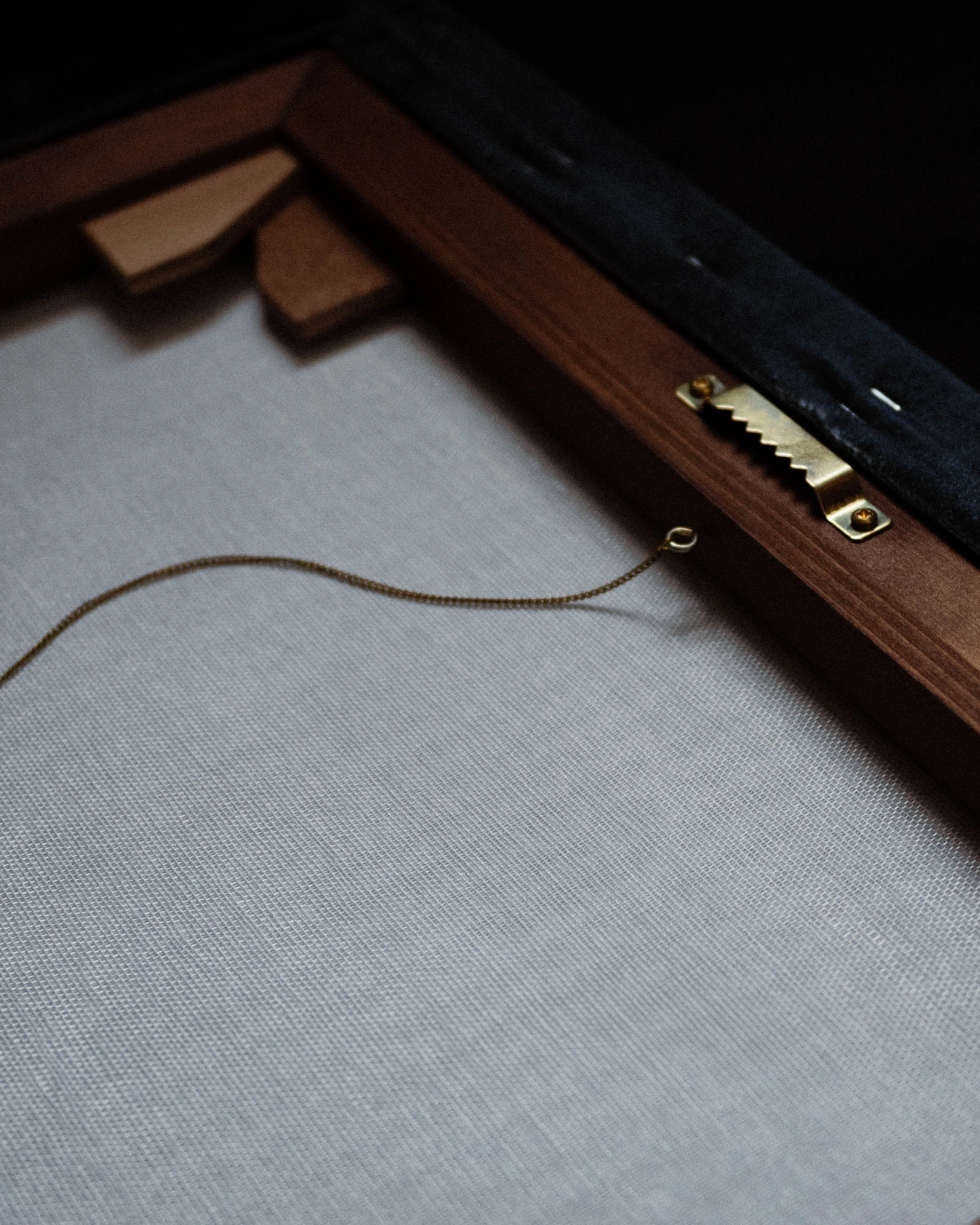 Close-up of the corner of a dark wooden picture frame with a gold hanging hook attached, on a textured gray surface.