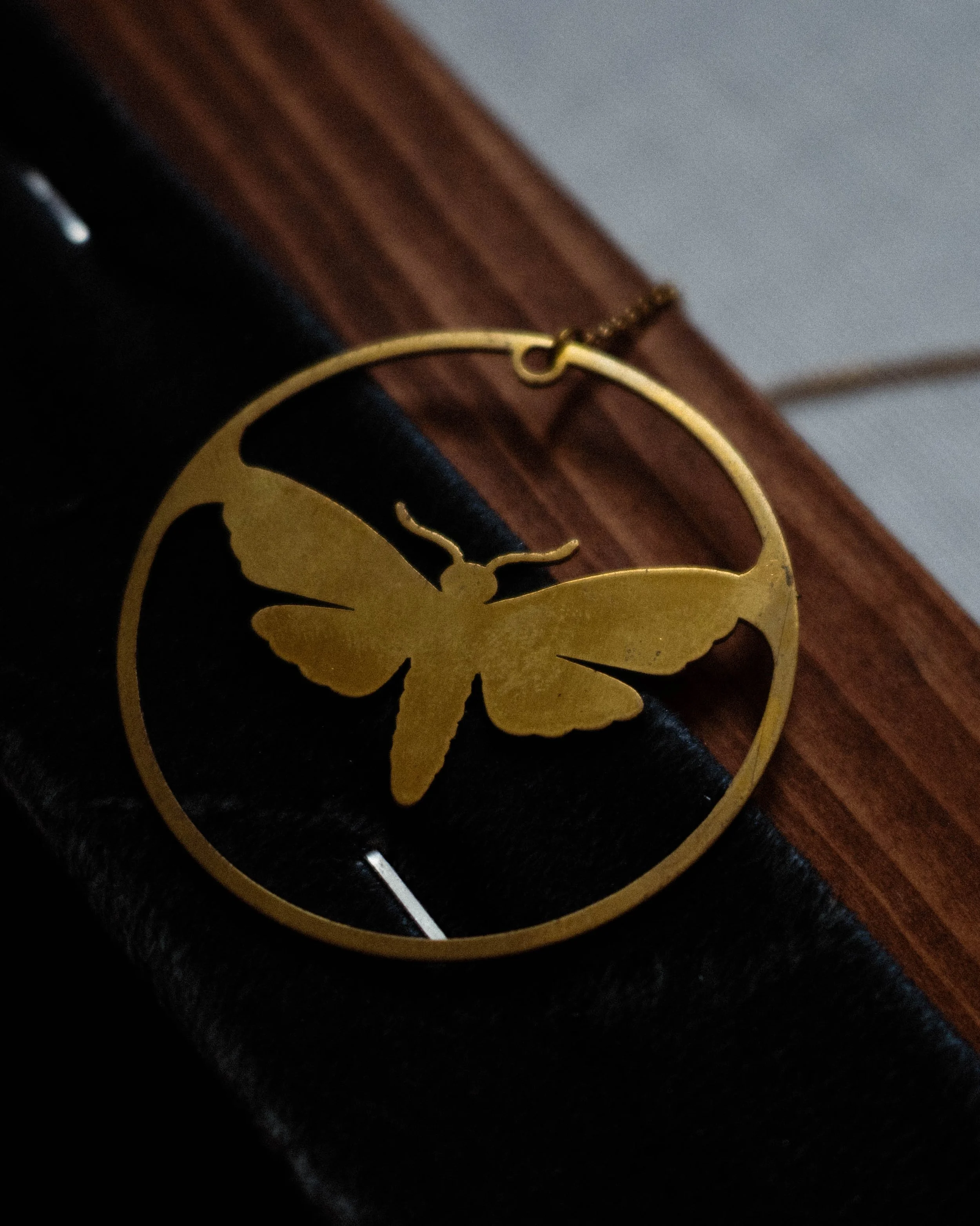 Close-up of a gold necklace with a butterfly-shaped pendant lying on a black fabric surface, with a wooden table in the background.