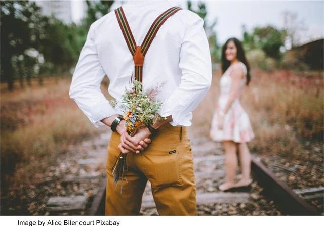 A boy holds flowers behind his back, ready to surprise a girl in the distance