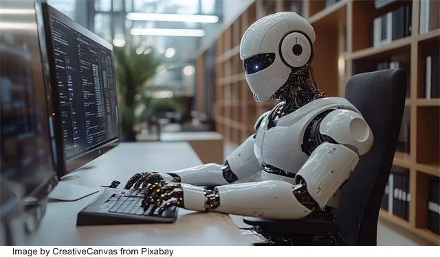Robot sitting at computer monitor with hands on keyboard
