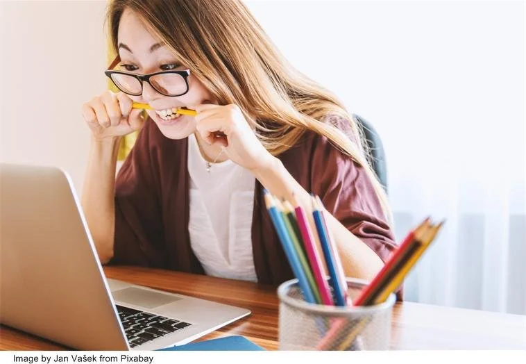 Female student bites pencil in frustration while looking at laptop screen