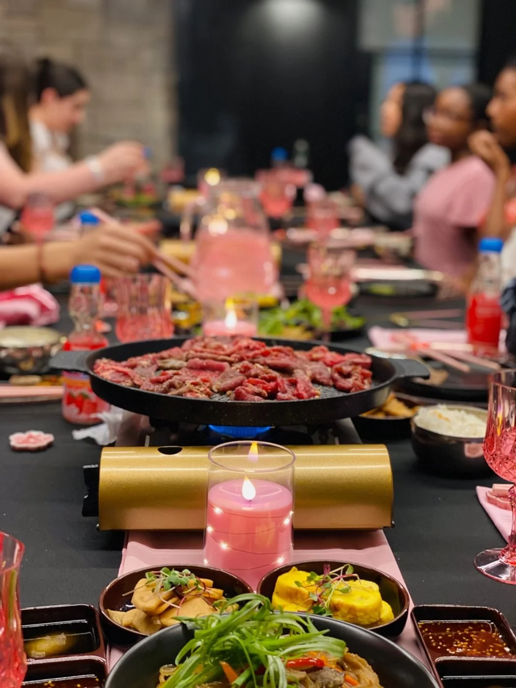 Guests at a tabletop Korean BBQ dinner with pink candles and place settings