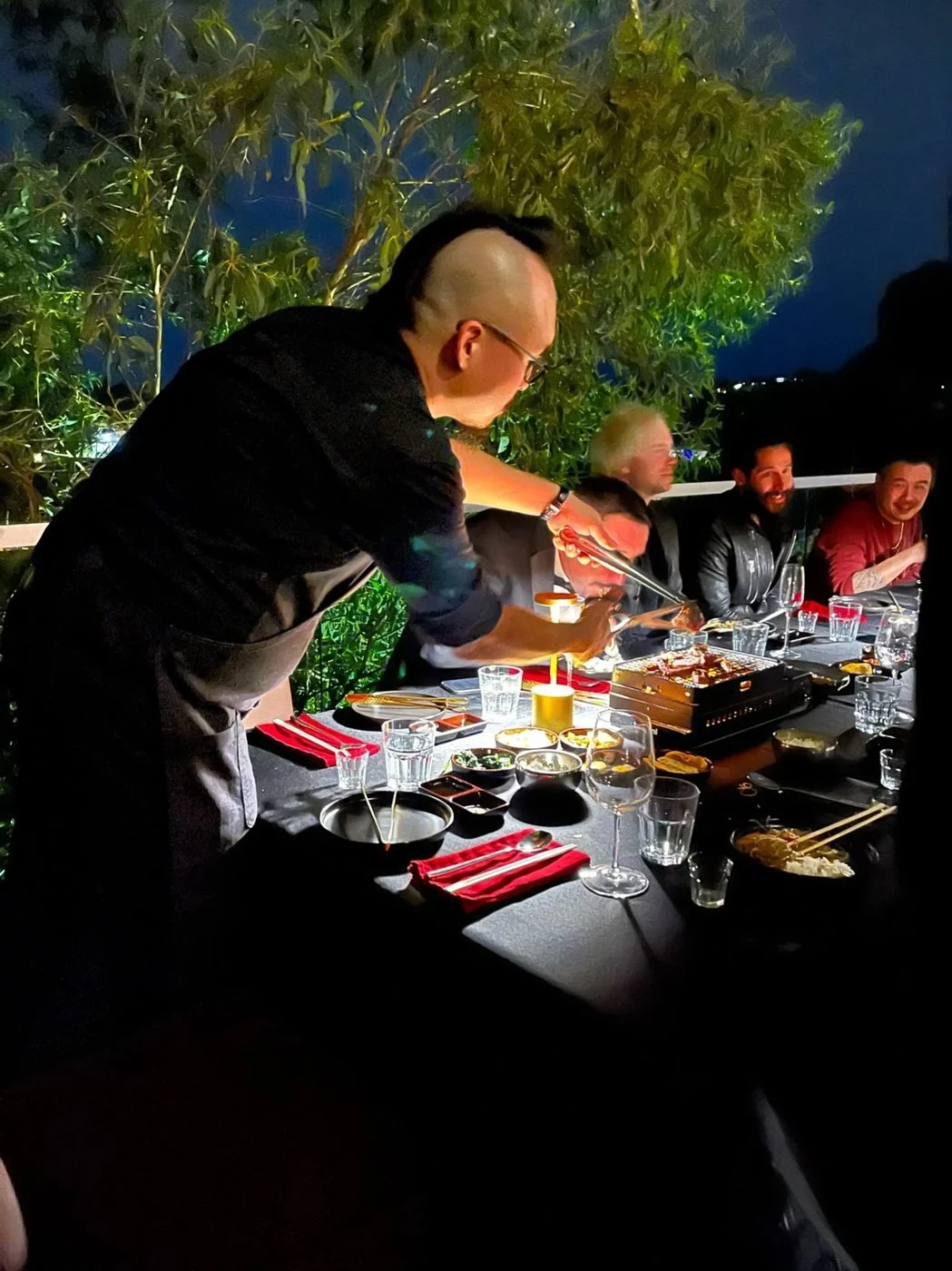 Chef grilling Korean BBQ tableside for guests at a private dinner at night