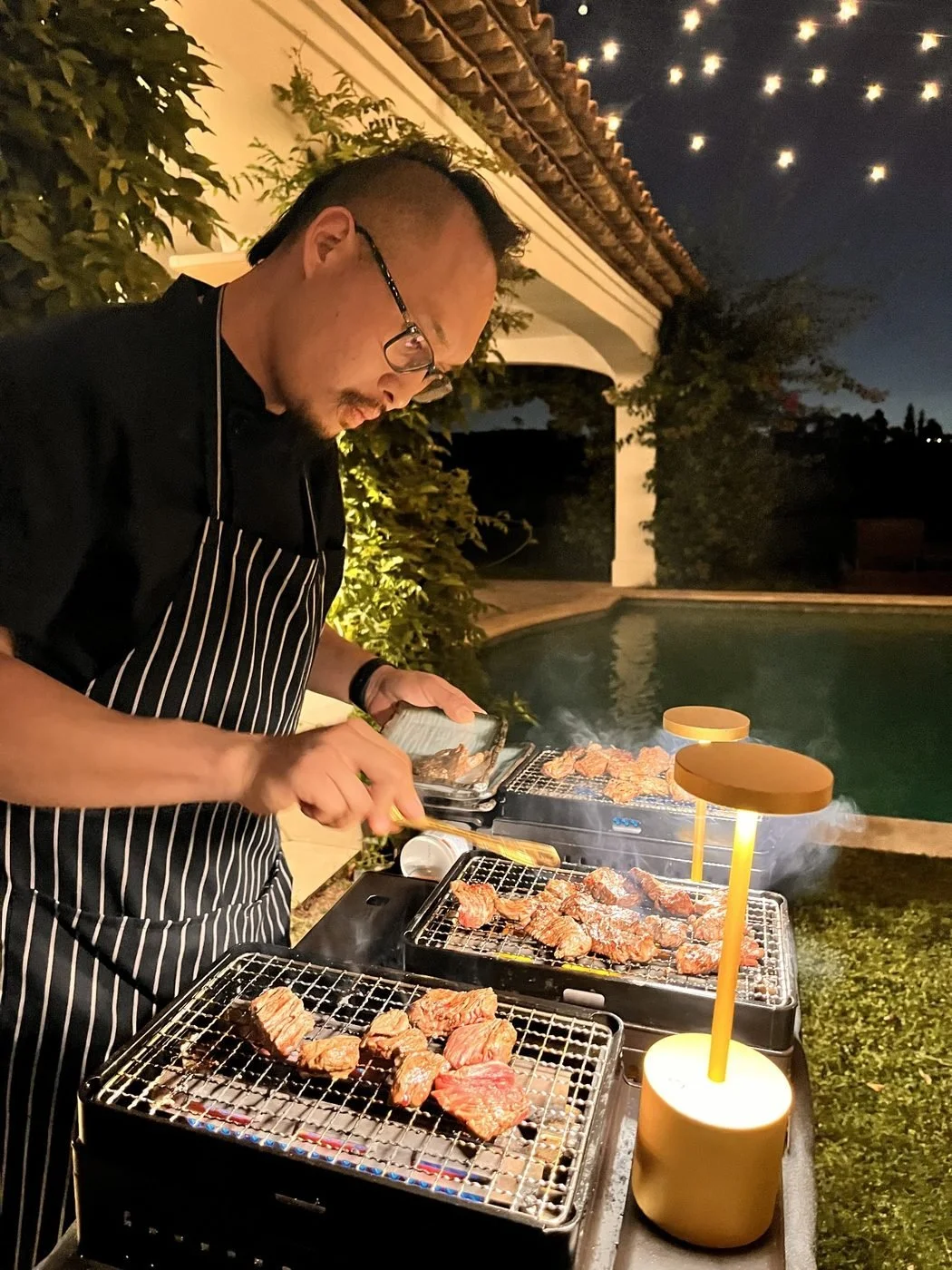 Private chef grilling Korean BBQ beside a pool at night
