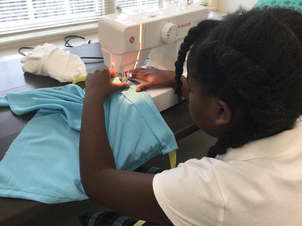 A girl sewing on a machine. She has dark skin and braids.