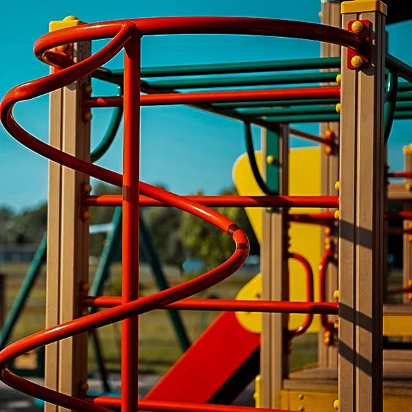 Colorful playground equipment with red, yellow, and teal bars in an outdoor park setting.