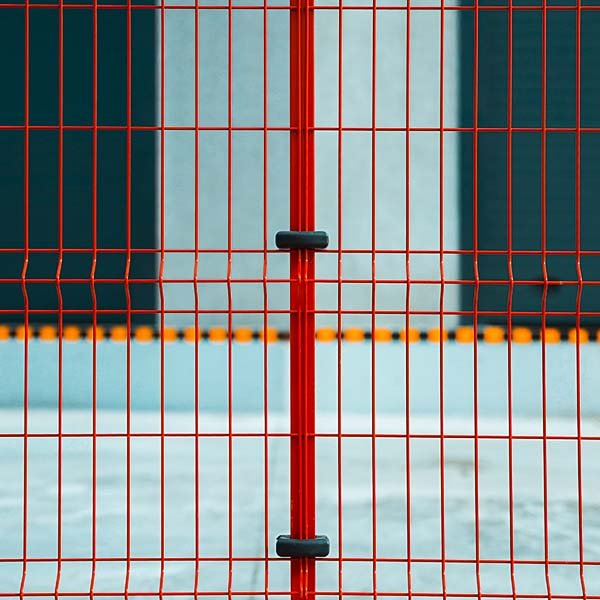 Close-up of a red metal fence with a black handle in the middle, and blurred skate park background.