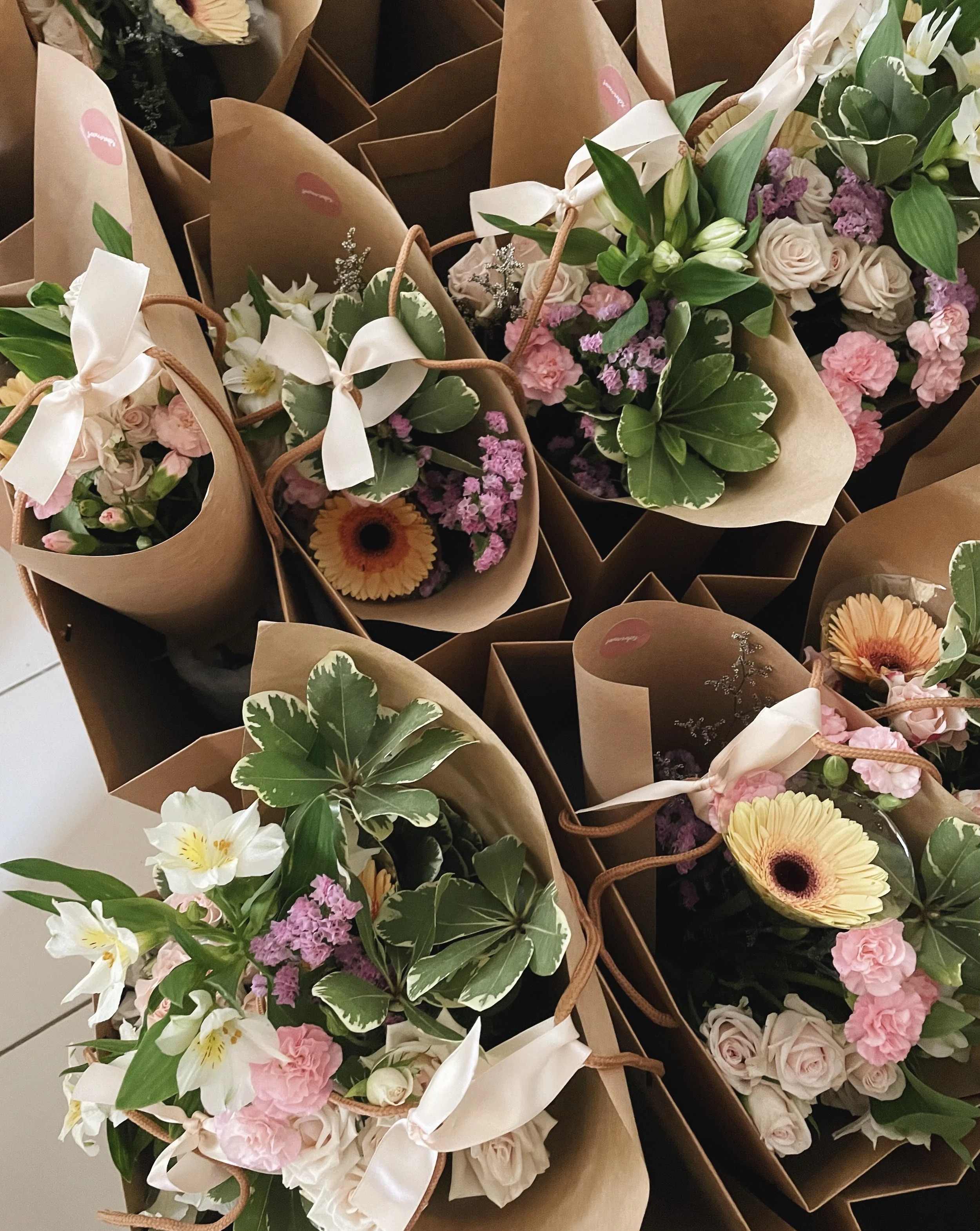 Multiple bouquets of mixed flowers wrapped in brown paper.