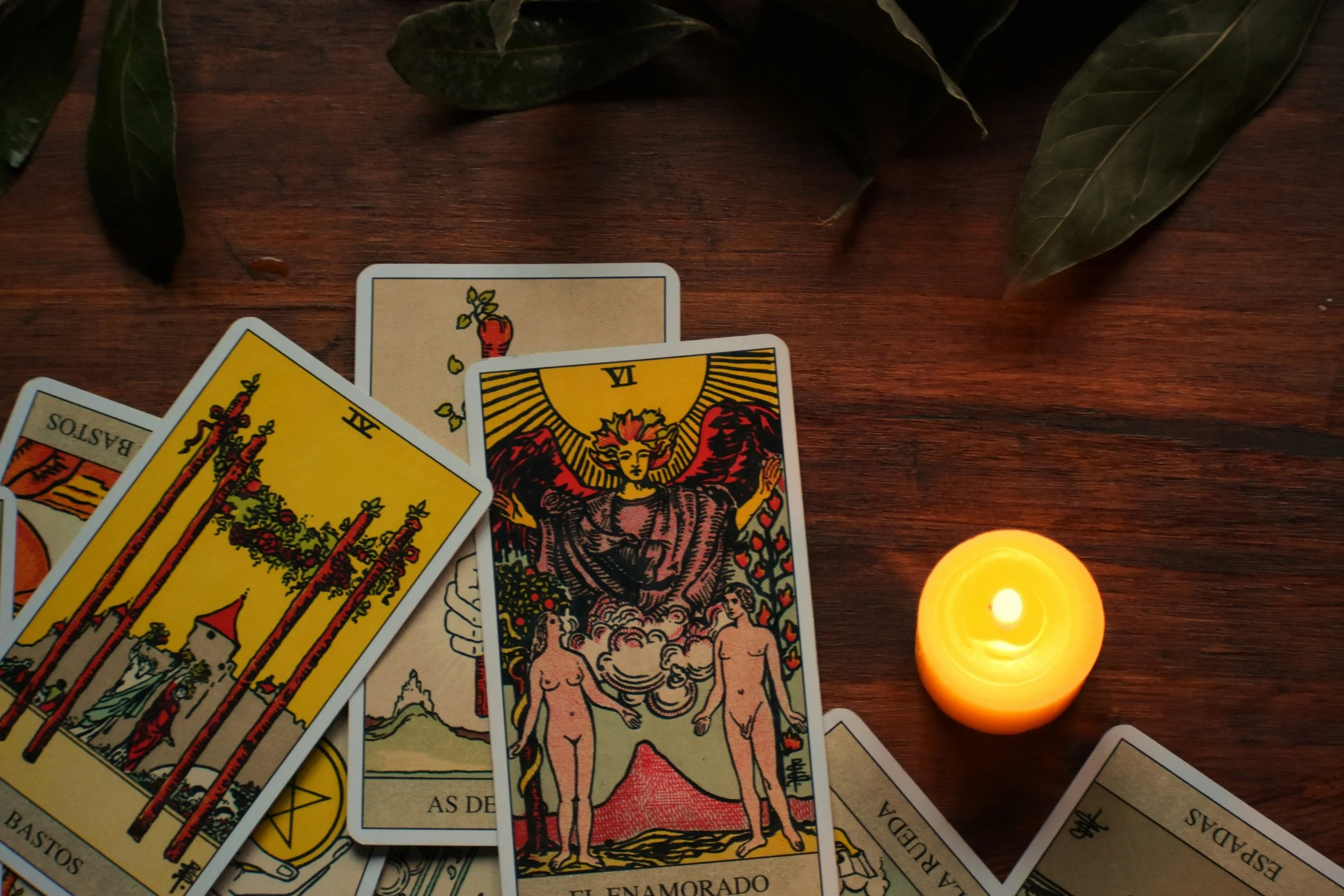 Tarot étalé sur une table en bois avec une bougie allumée et des feuilles vertes en arrière-plan.