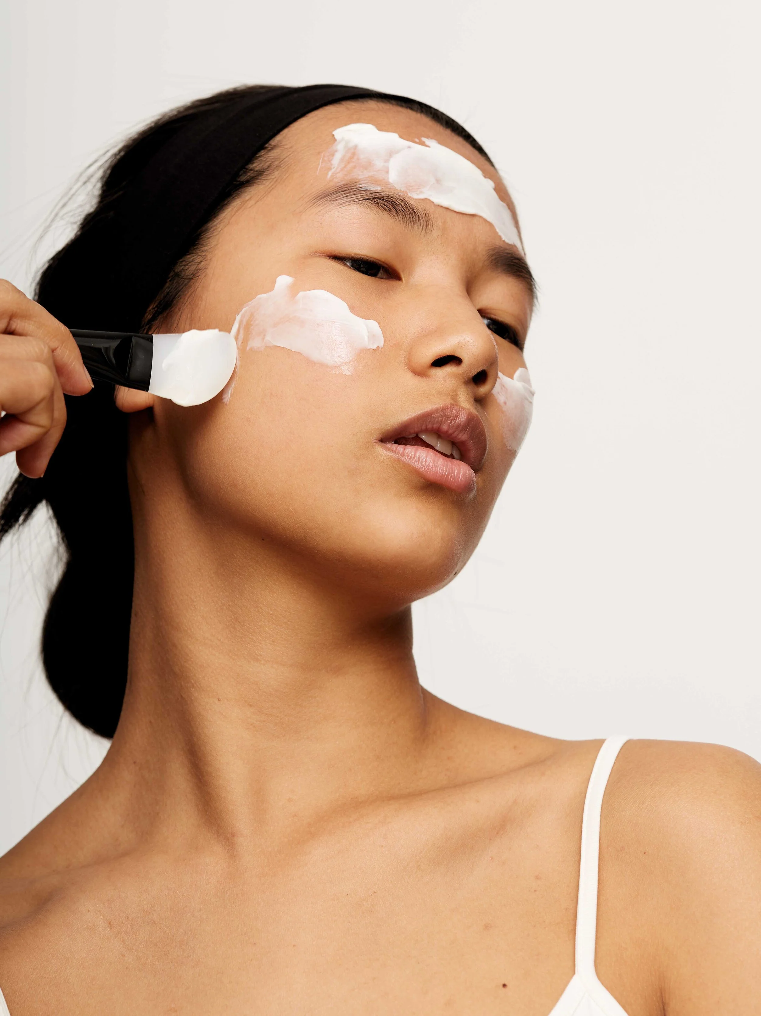 Eine junge Frau trägt eine Gesichtsmaske auf und verwendet einen Pinsel, um die Maske auf ihr Gesicht aufzutragen.