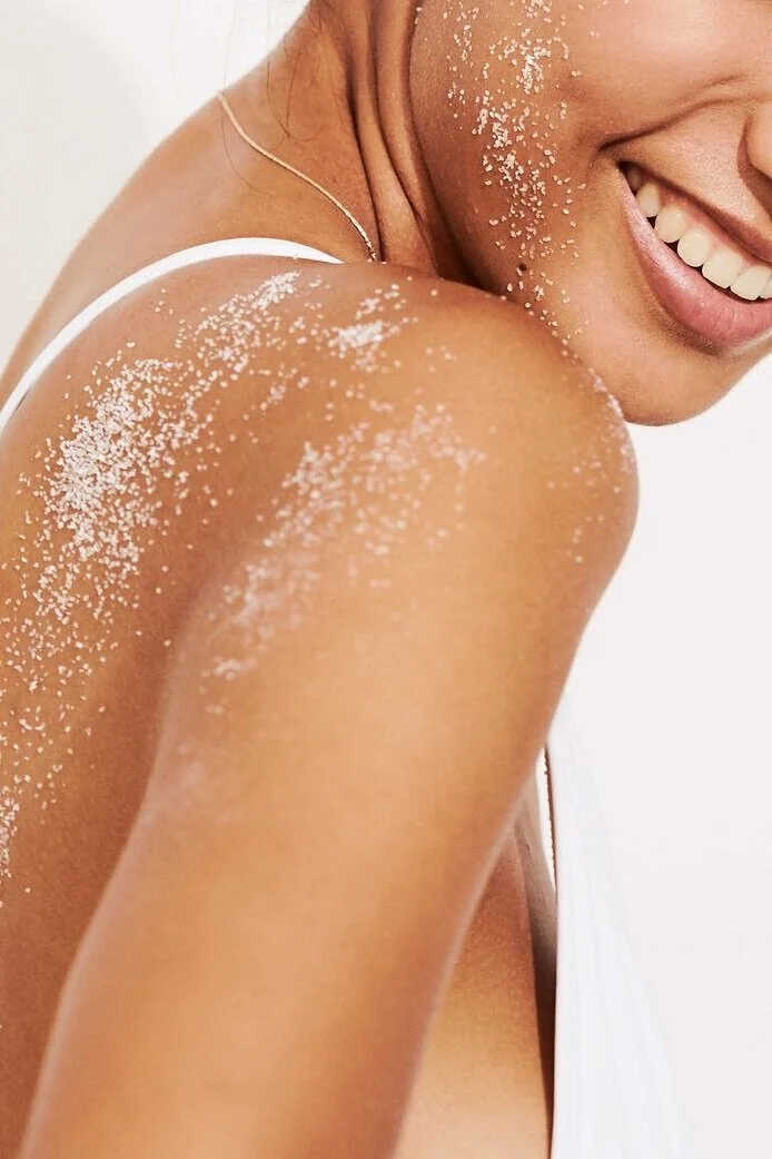 Nahaufnahme einer lachenden Frau, die auf ihrer Schulter und Arm mit Sand bedeckt ist.
