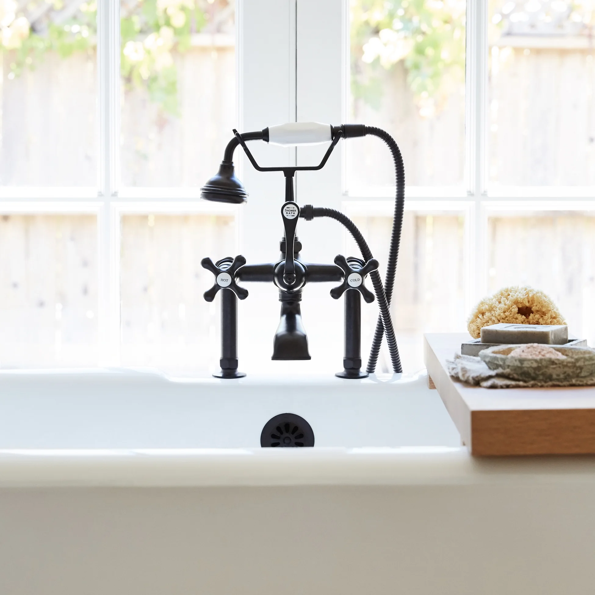 Mezcladora de baño negra con ducha a la izquierda, cerca de una ventana y junto a una mesa de jabón y esponjas.