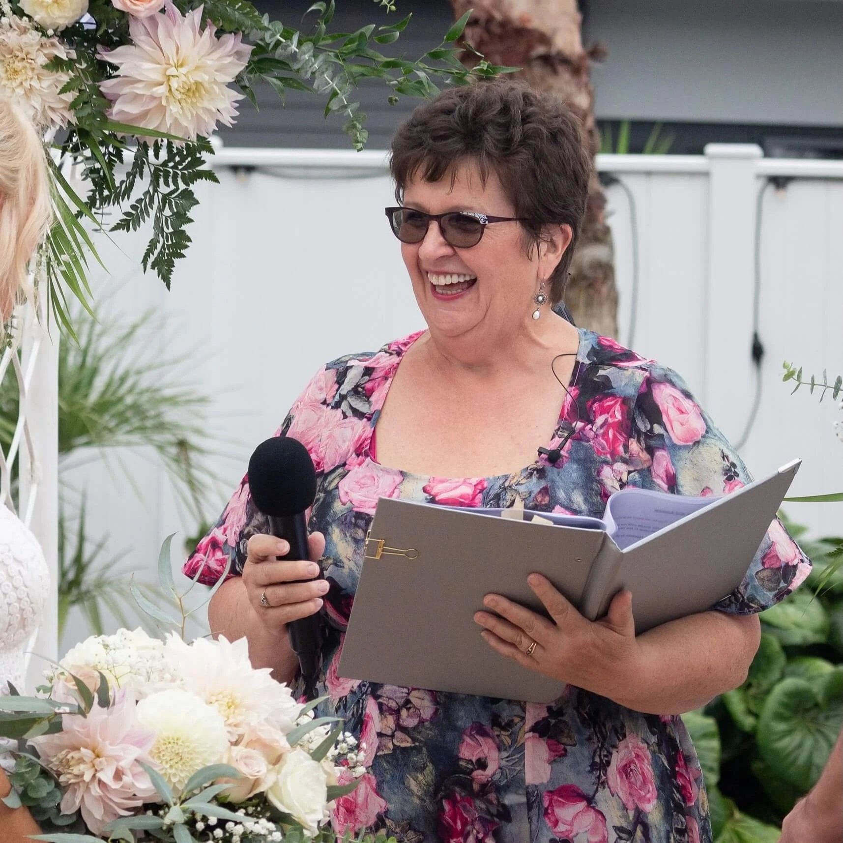 Debbie Woodfield holding a microphone and laughing during a wedding ceremony